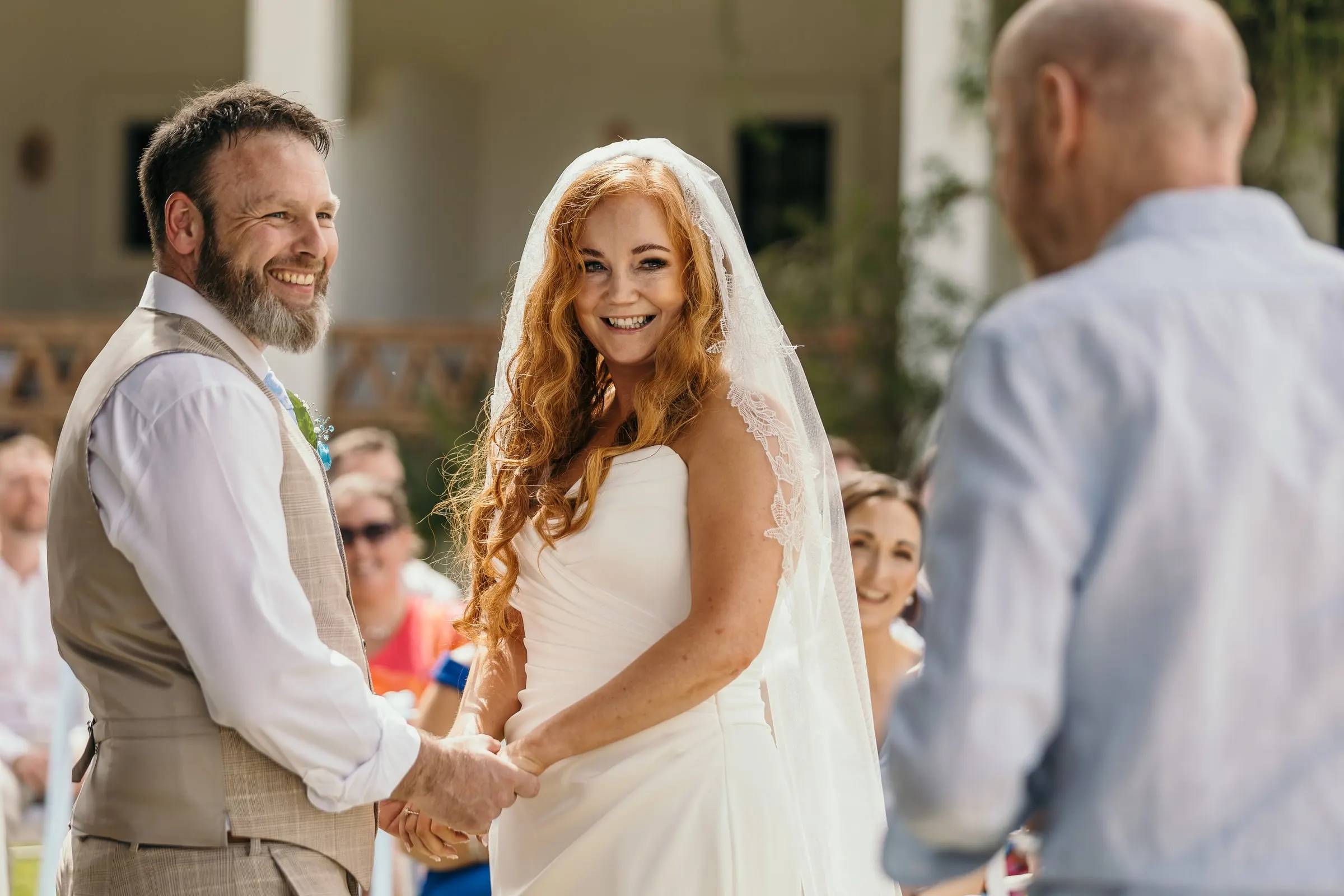 Bride and groom holding hands and laughing in front of the officiant, Hacienda San José