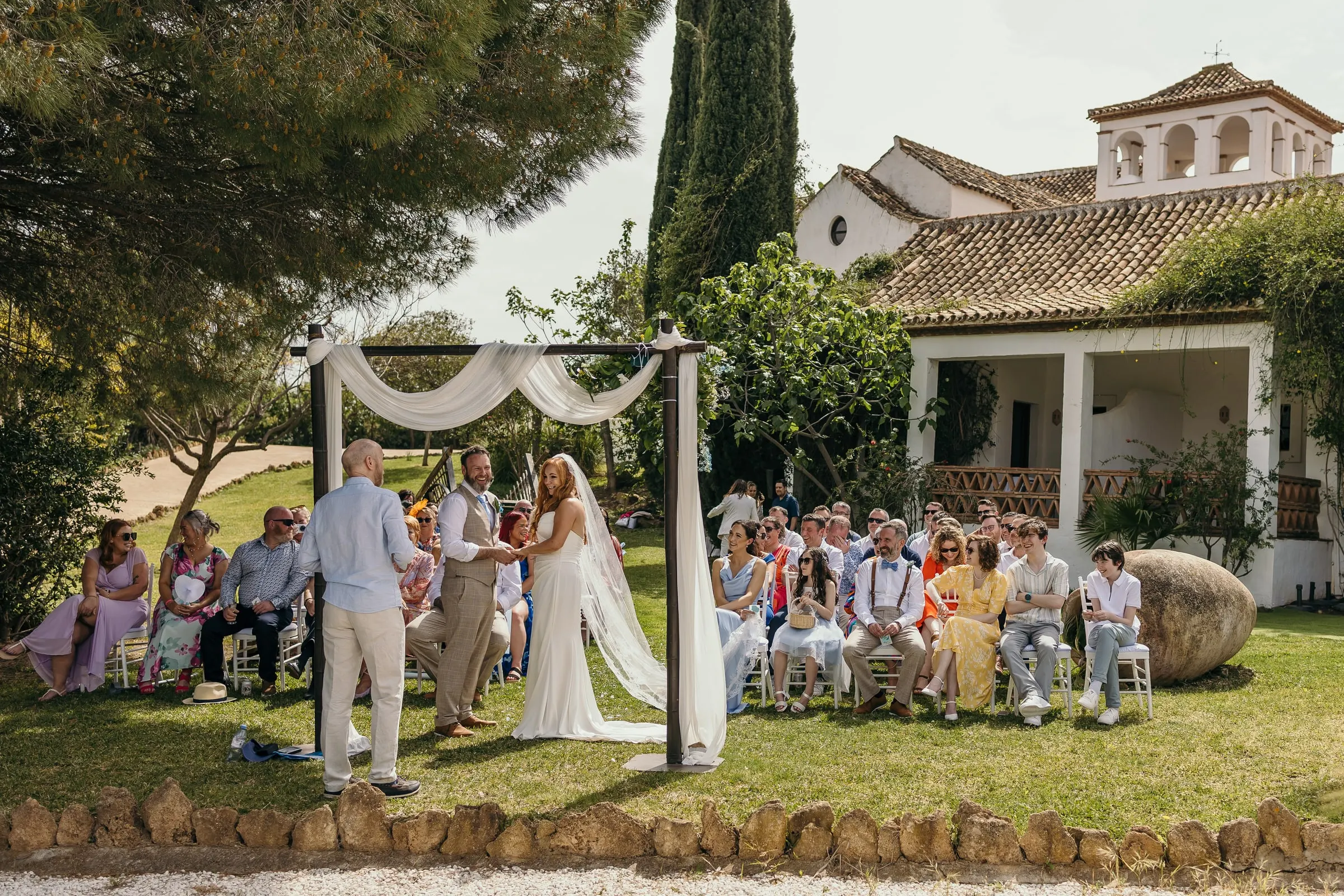 Garden ceremony under a white draped arch with the hacienda bell tower behind, Hacienda San José, Mijas