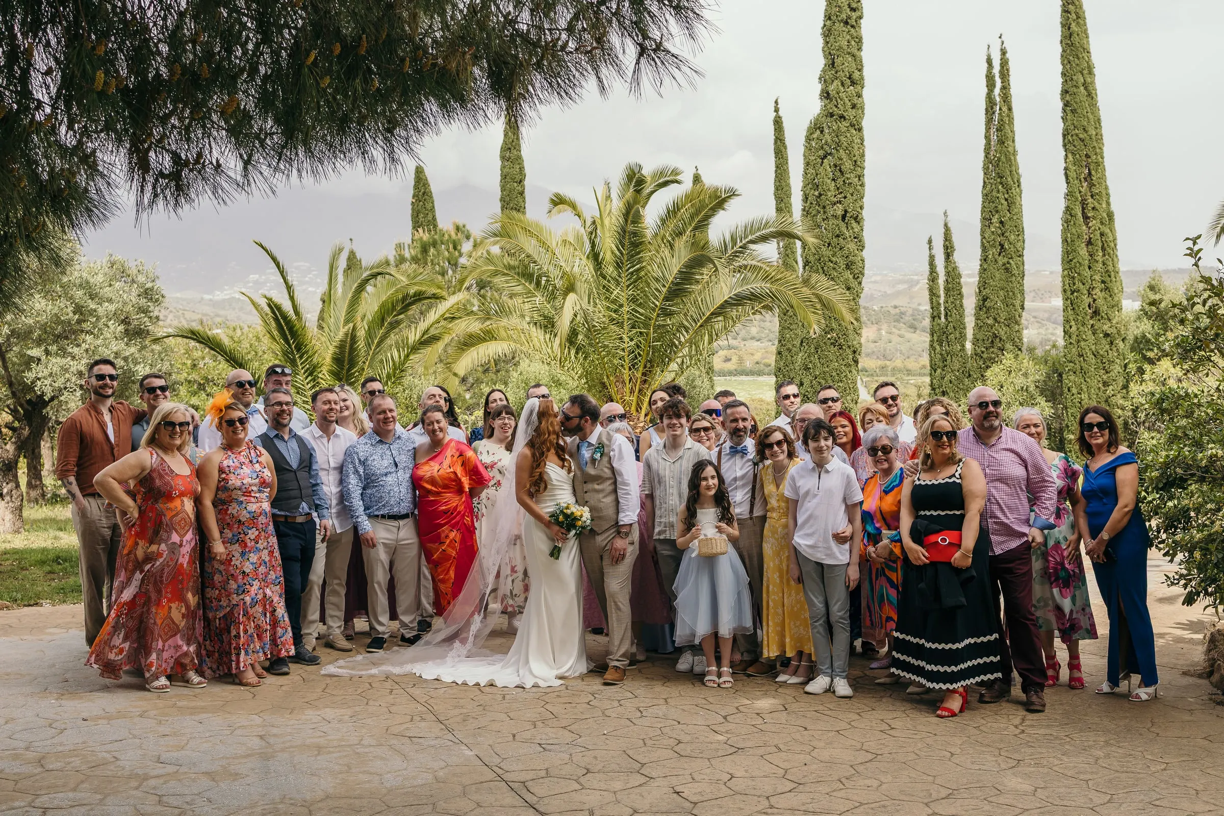 Group photo of all the wedding guests among palms and cypresses at Hacienda San José