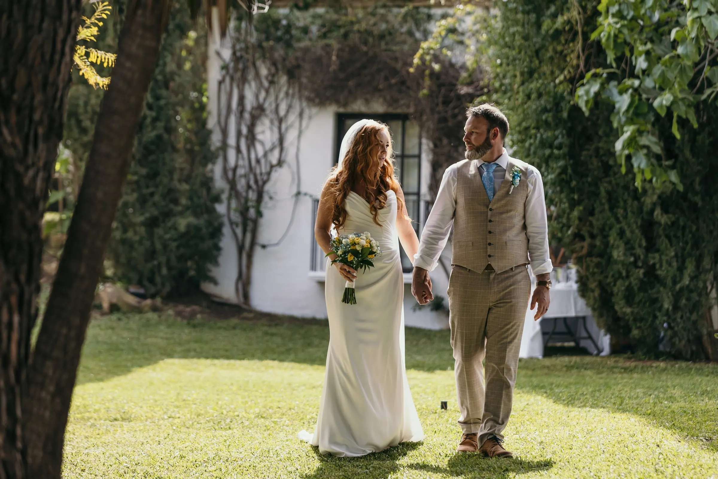 Couple walking hand in hand across the shaded lawn of Hacienda San José