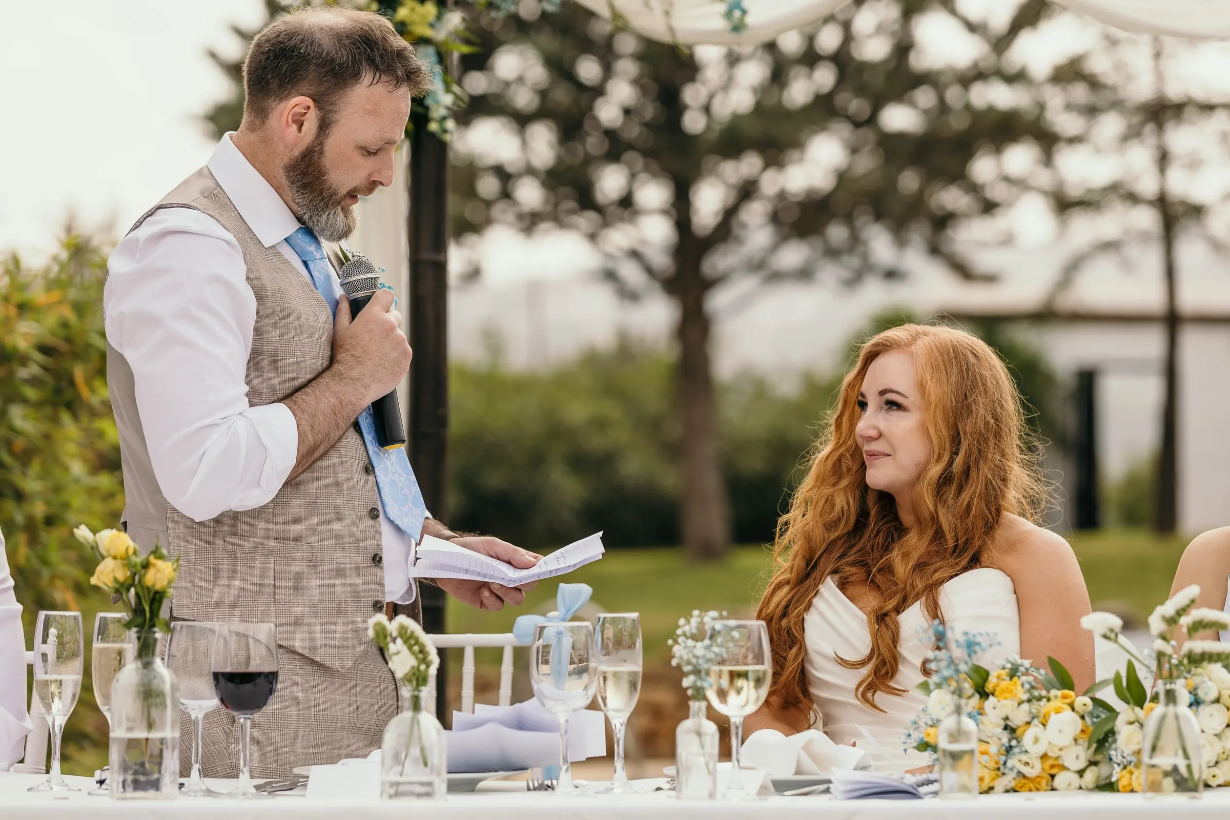 Groom giving his speech with a microphone as the bride looks on, reception in Mijas