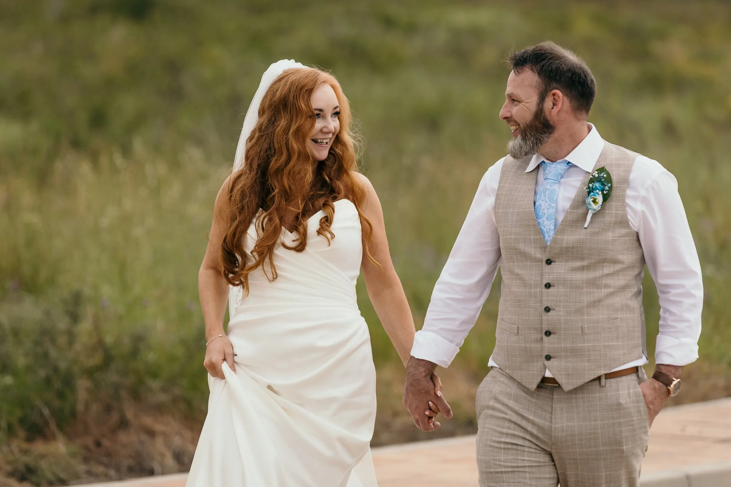 Bride lifting her dress and laughing as the couple walk through the long grass near Hacienda San José