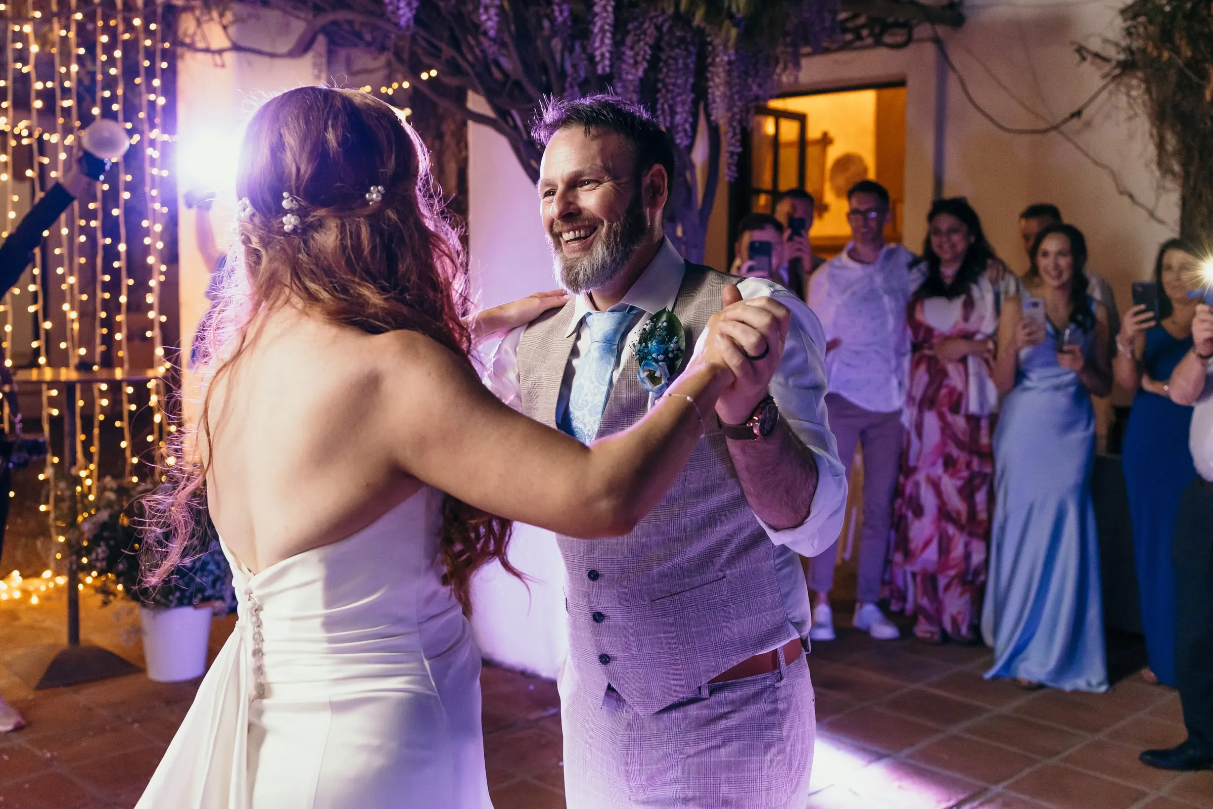 Primer baile en el patio iluminado de morado mientras los invitados graban con el móvil, Mijas