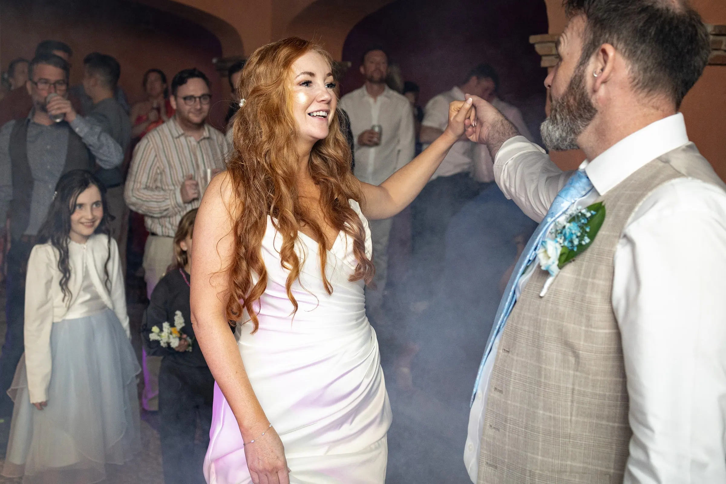 Bride and groom dancing in the smoke as the flower girl watches, wedding party in Mijas