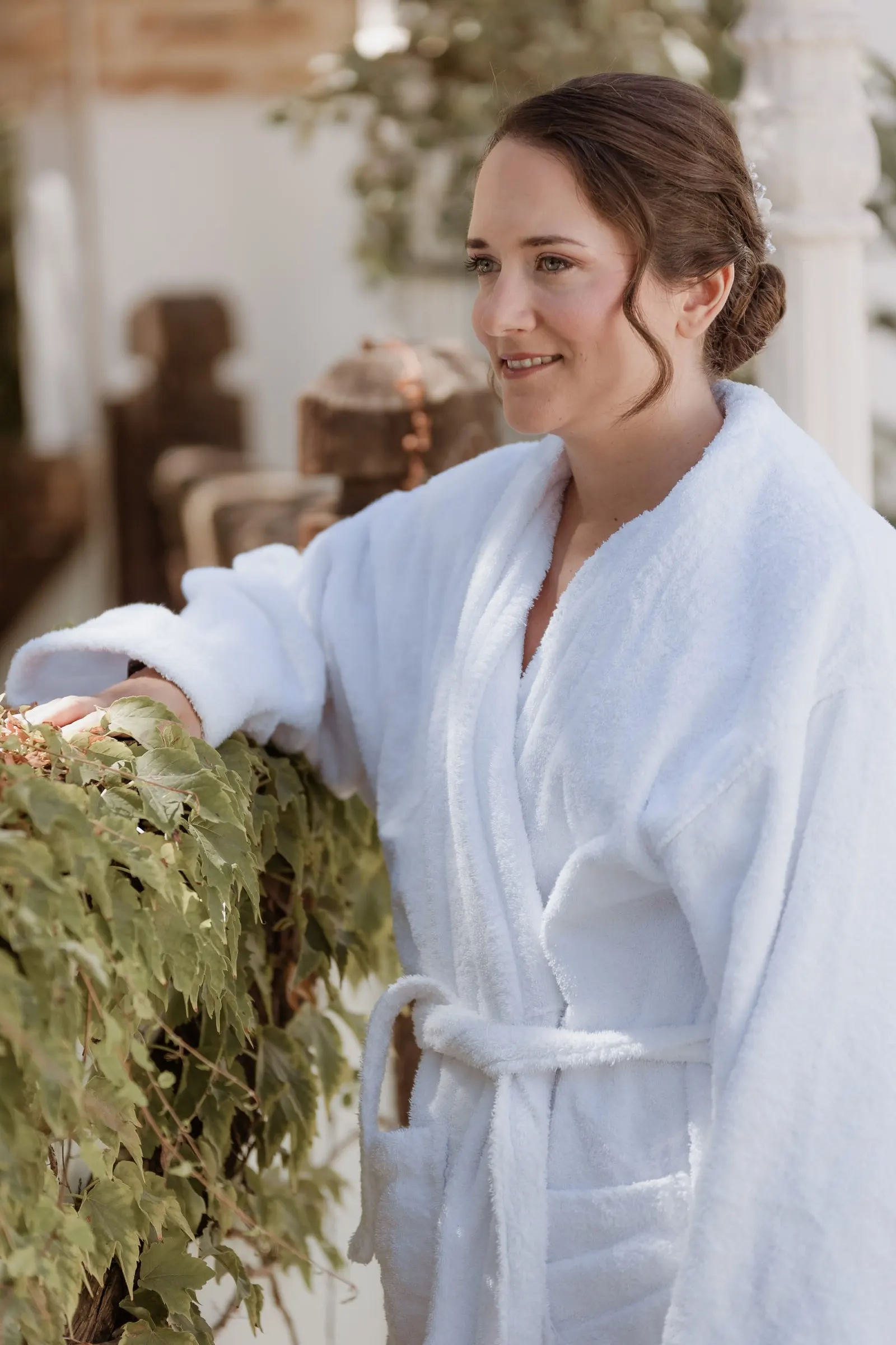 La novia en albornoz blanco sonríe junto a la ventana en Los Pilares de Ronda
