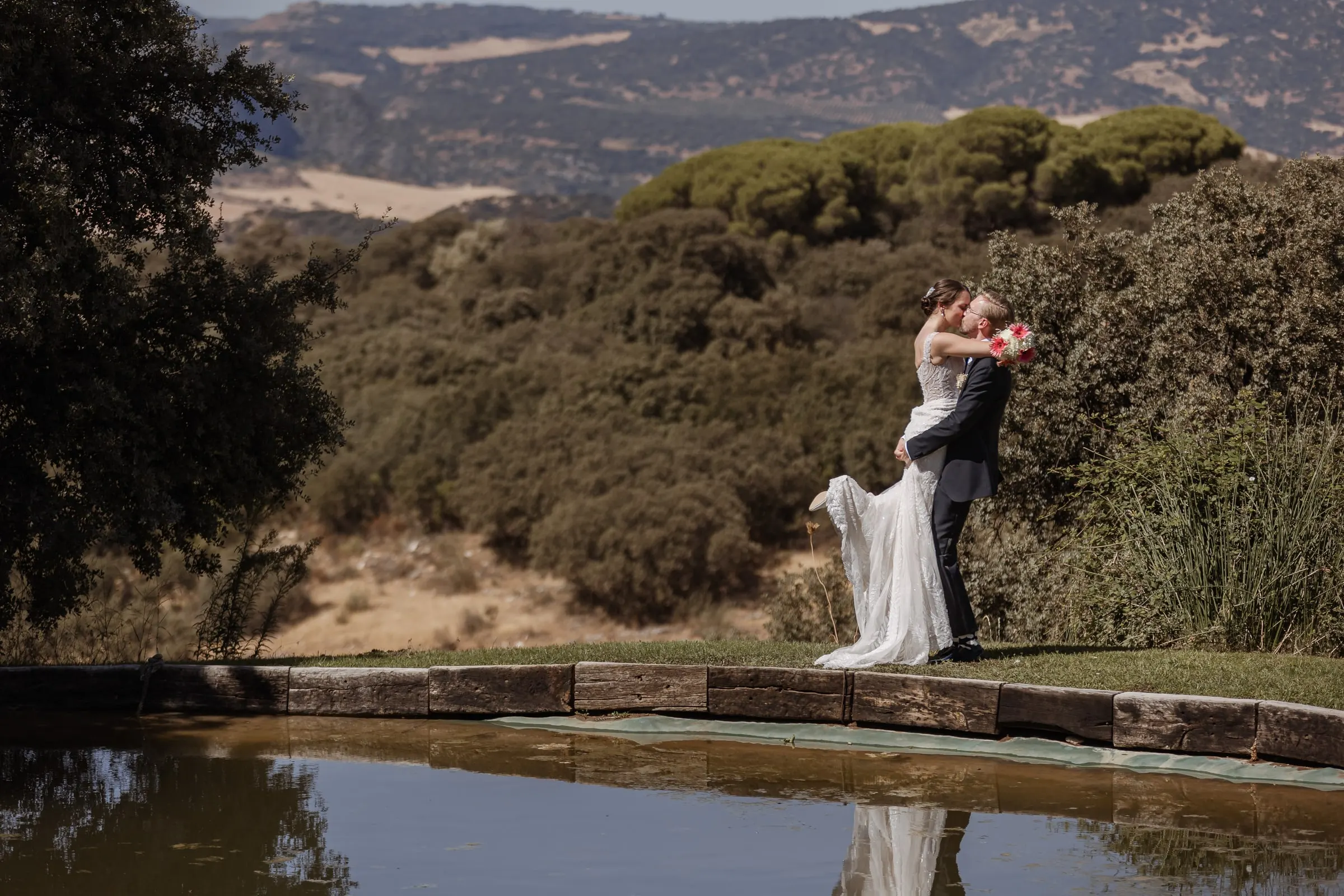 Groom lifting the bride by the pond with the hills of Ronda behind