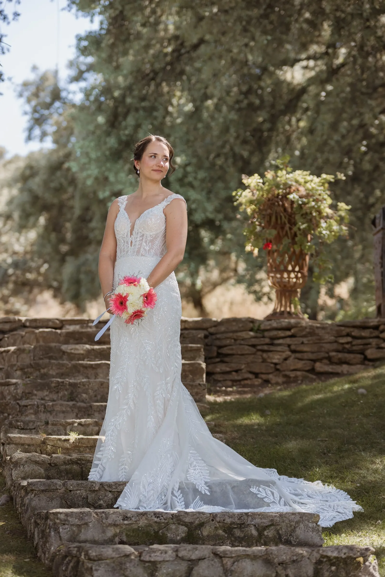La novia con su ramo rosa en los escalones de piedra junto a un jarrón de flores en Los Pilares de Ronda