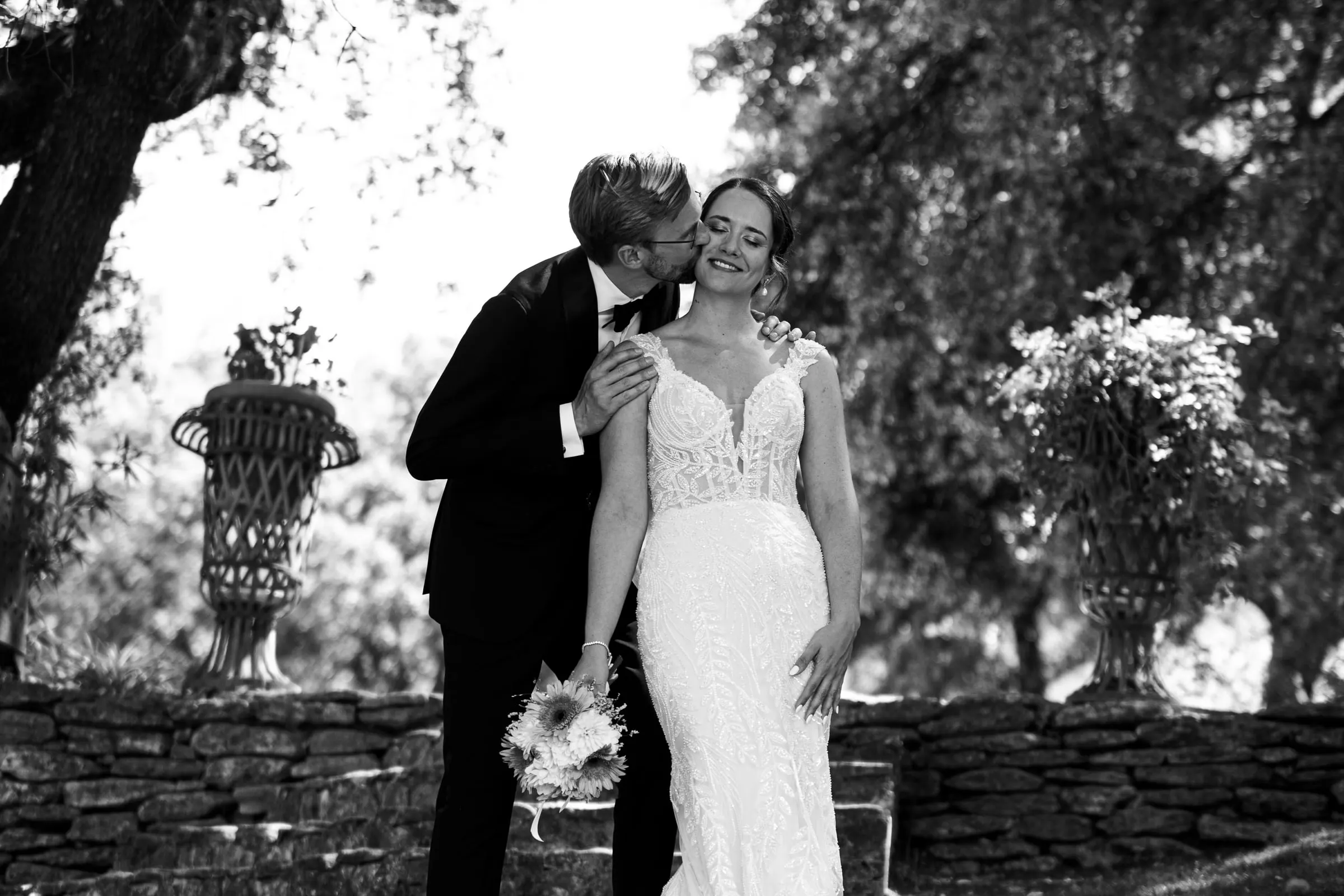 Foto en blanco y negro del novio besando la mejilla de la novia en el jardín