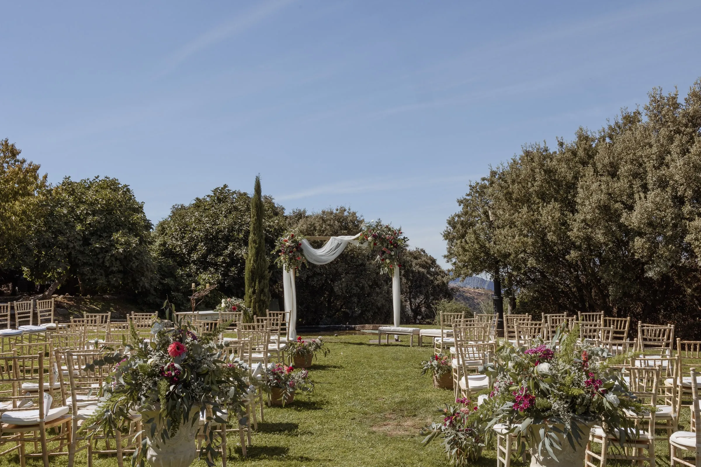 Ceremony set on the lawn at Los Pilares de Ronda: gold chairs, flowers and a draped arch