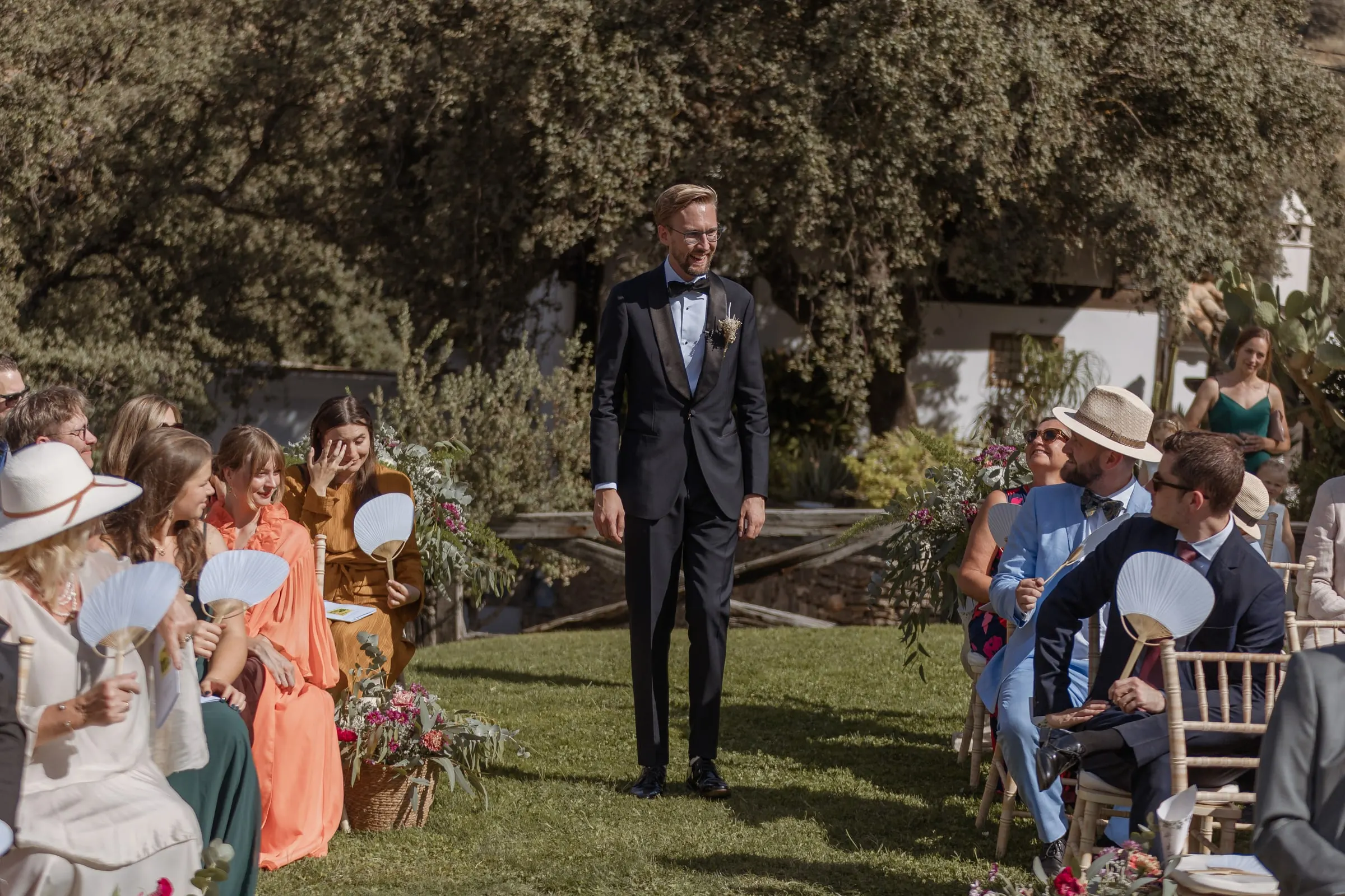El novio espera al final del pasillo mientras los invitados se abanican