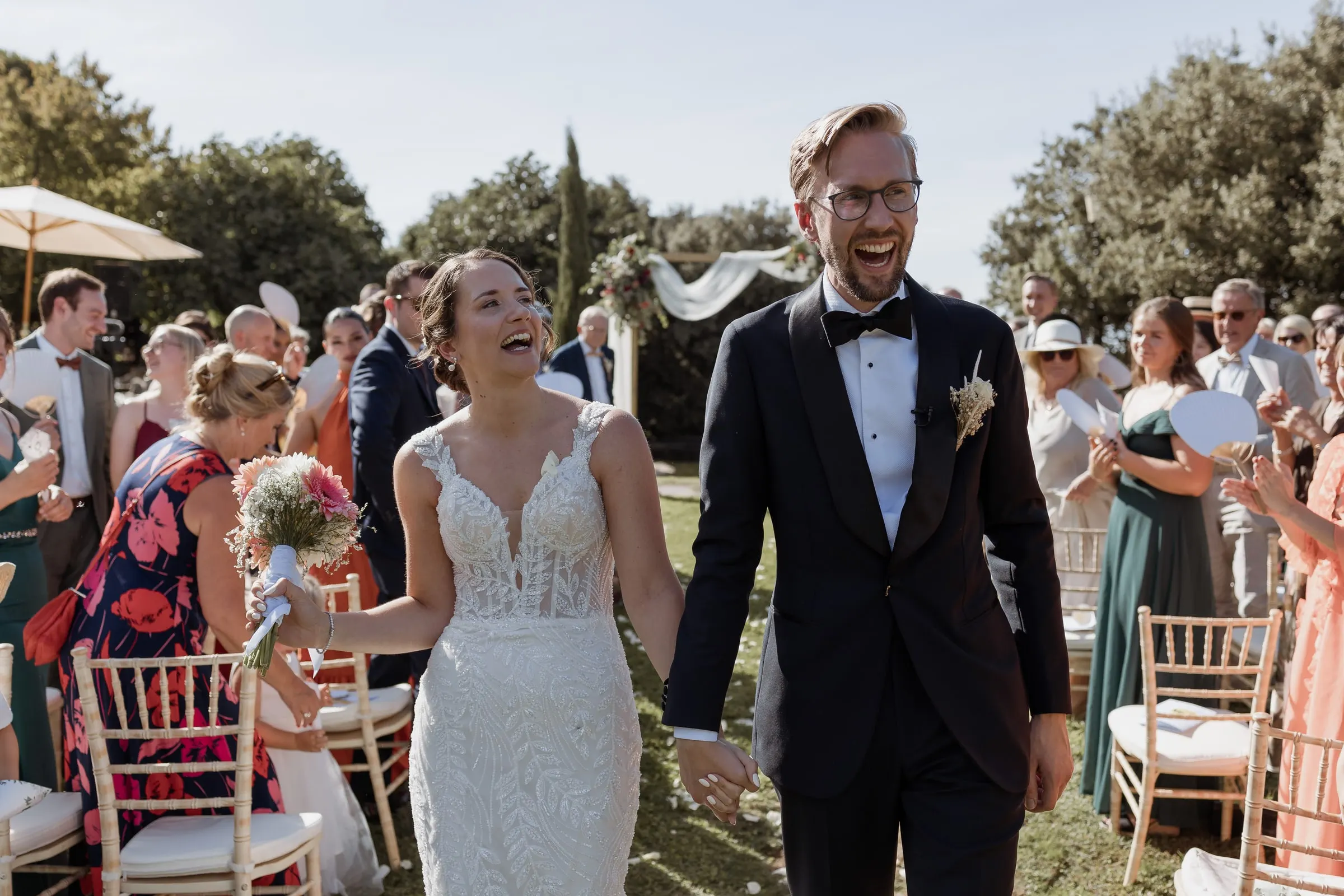 Los novios se ríen al salir de la ceremonia entre sus invitados