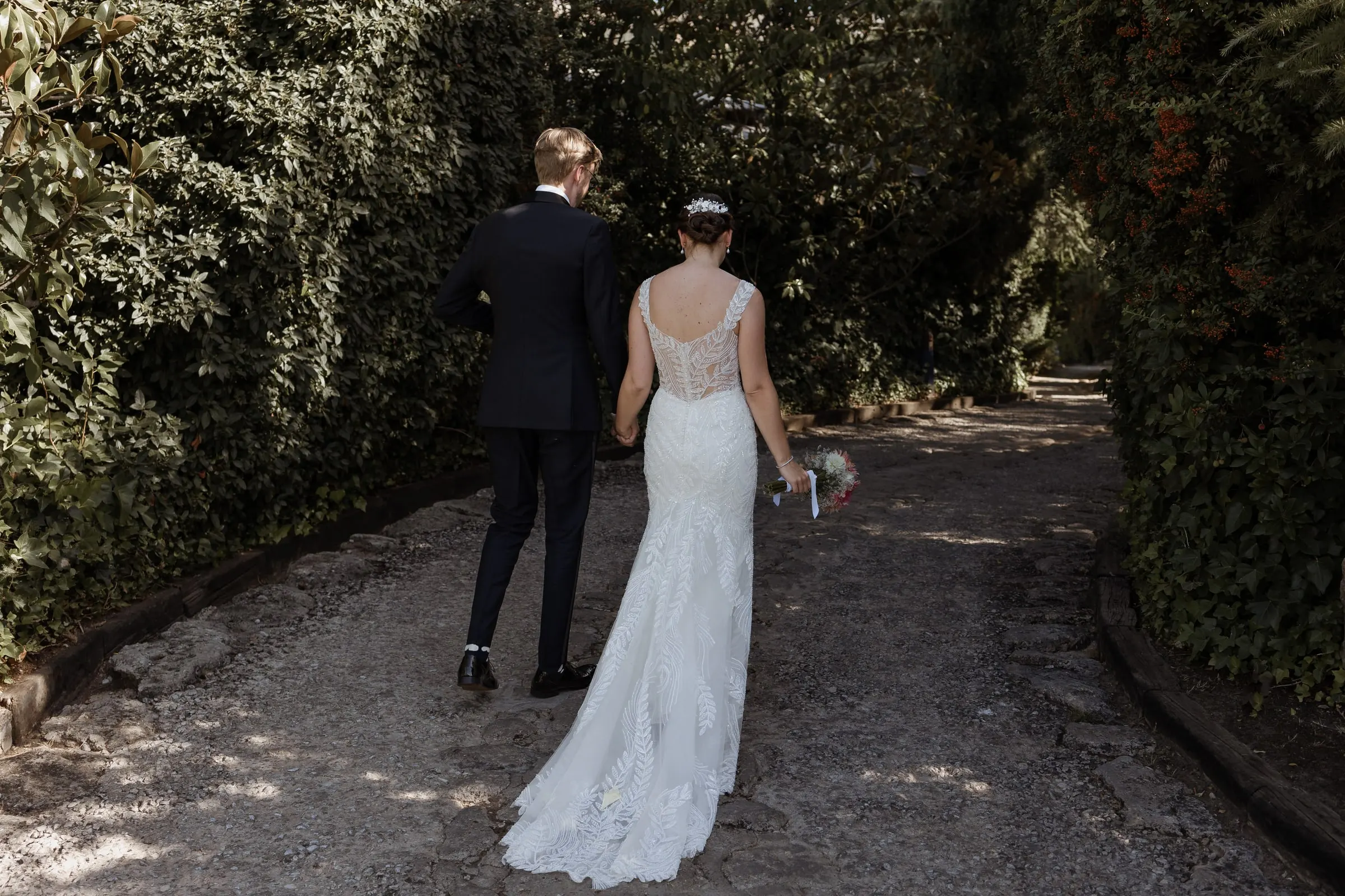 Los recién casados se alejan por un camino de grava a la sombra