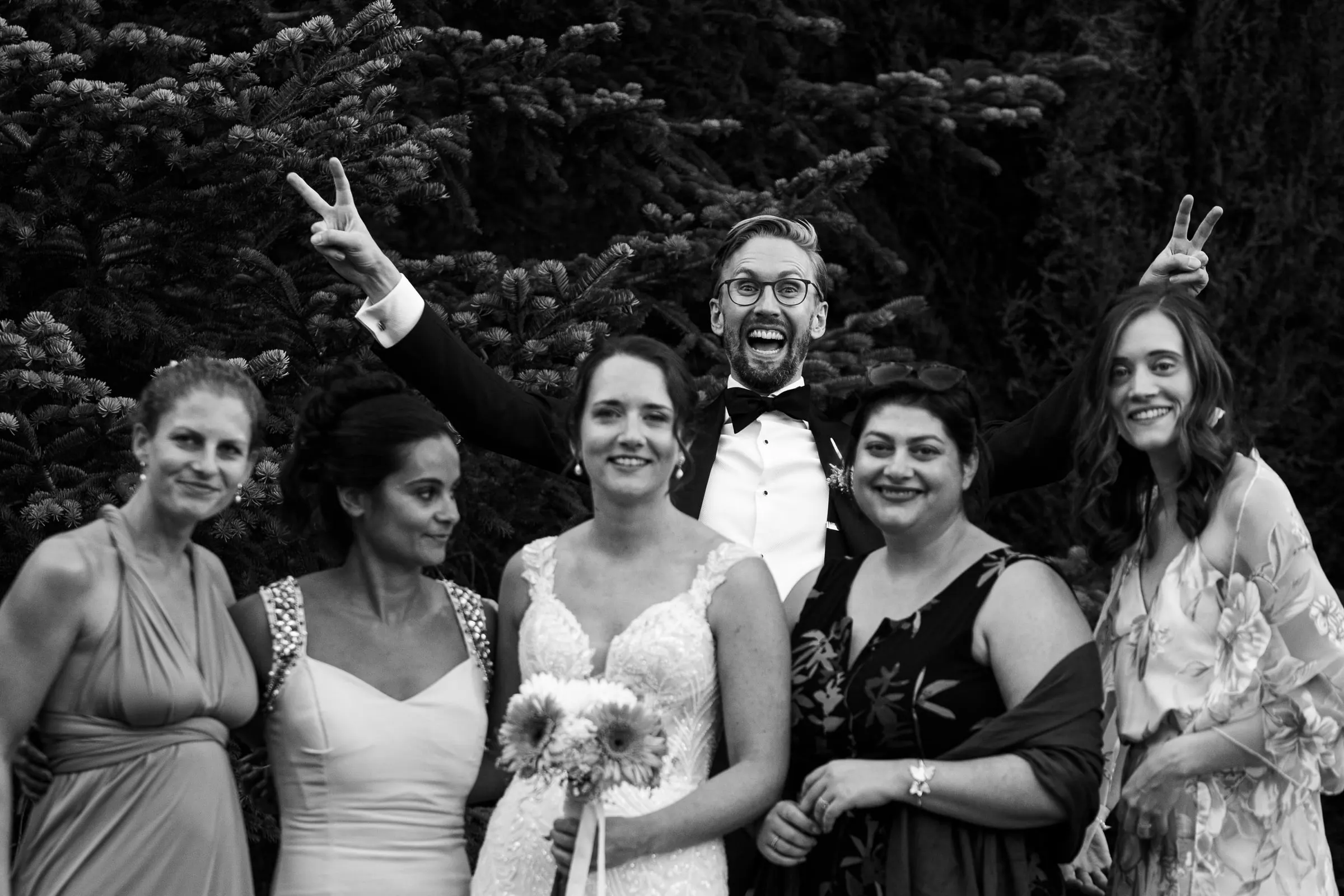 Foto en blanco y negro de la novia con sus amigas mientras el novio se cuela detrás