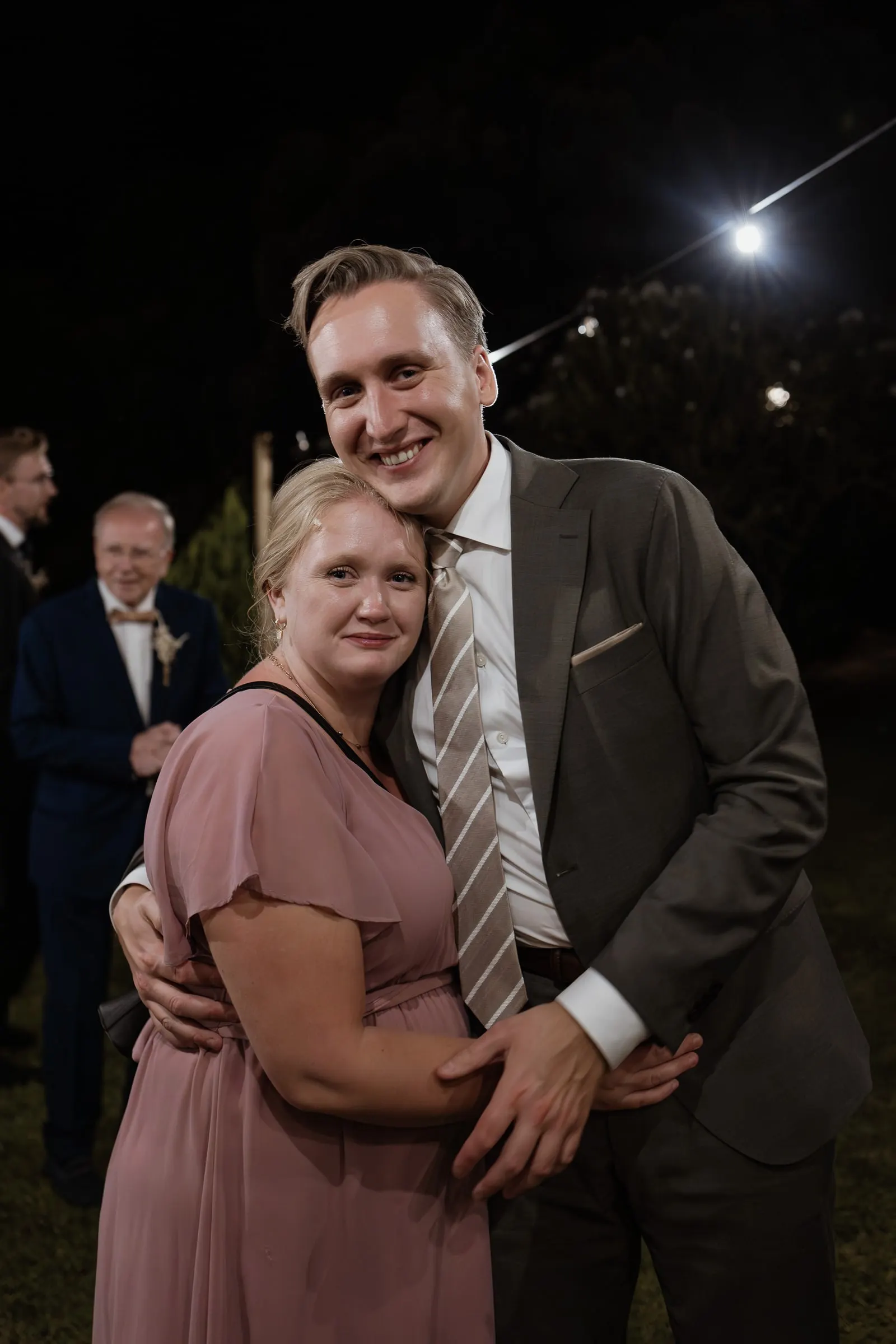 Una pareja de invitados abrazada posando en la pista de noche