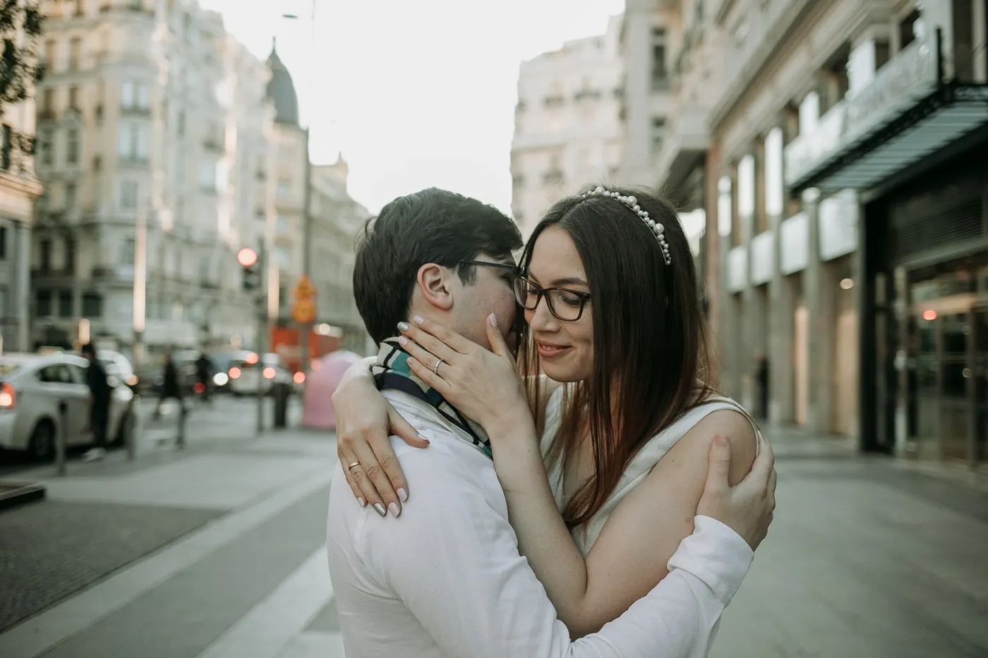 La novia, con gafas, besa la mejilla del novio en una acera de Madrid