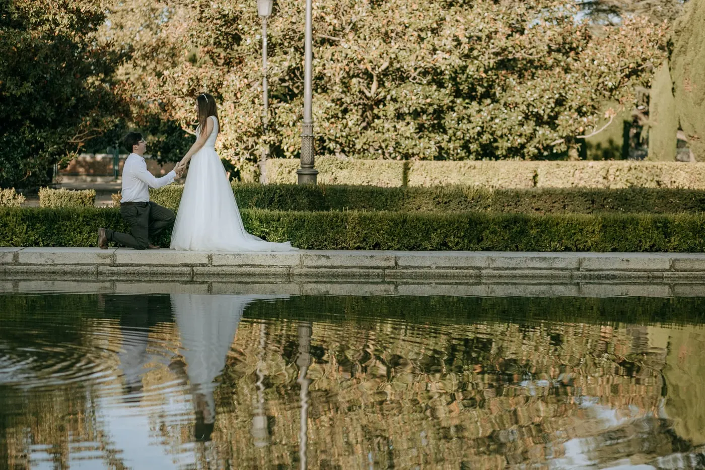 El novio, arrodillado ante la novia al borde de un estanque del jardín
