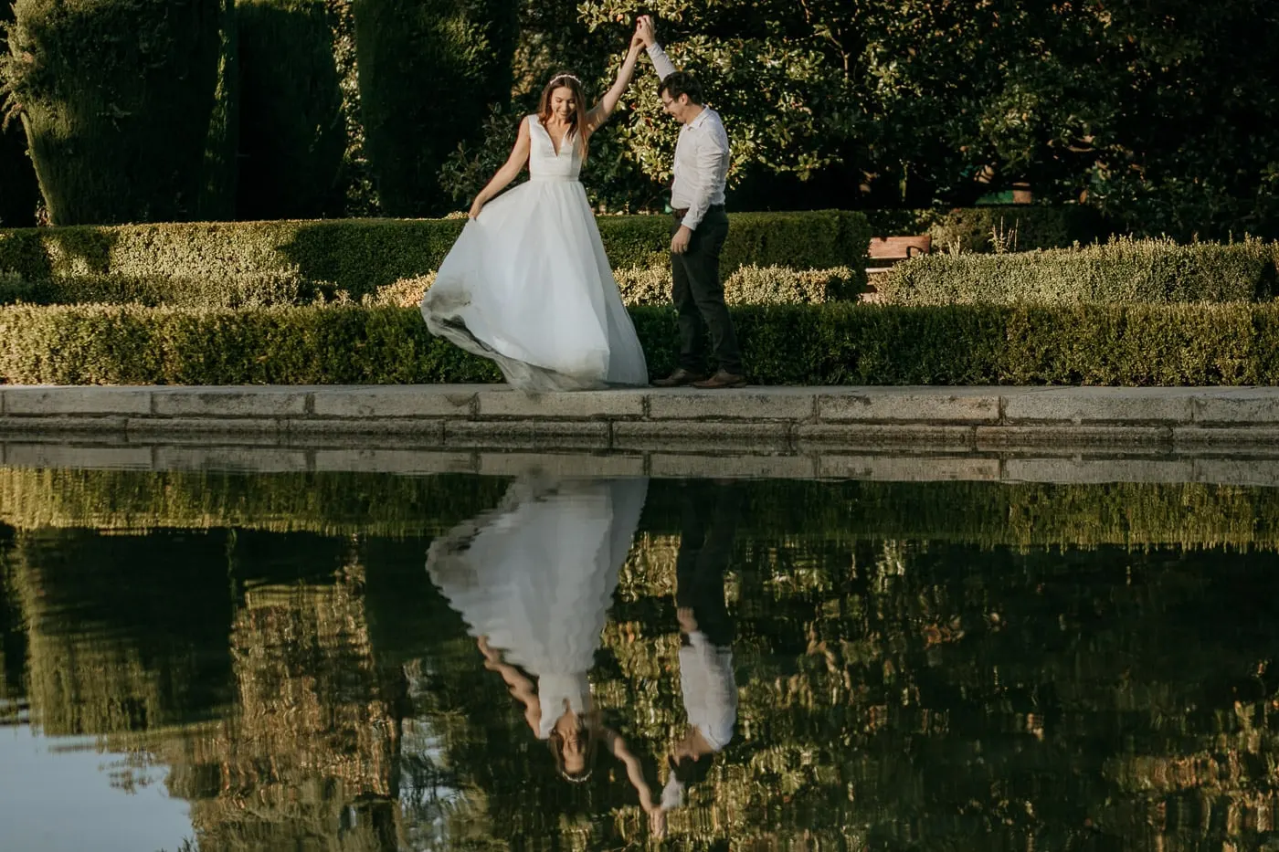 La novia gira con su falda de tul junto al estanque, reflejada en el agua