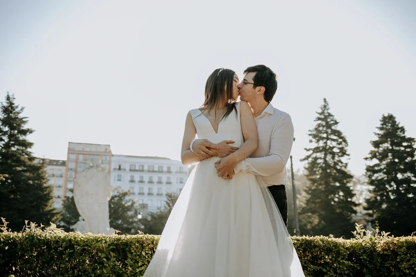 Los novios se besan sobre un seto recortado con edificios detrás