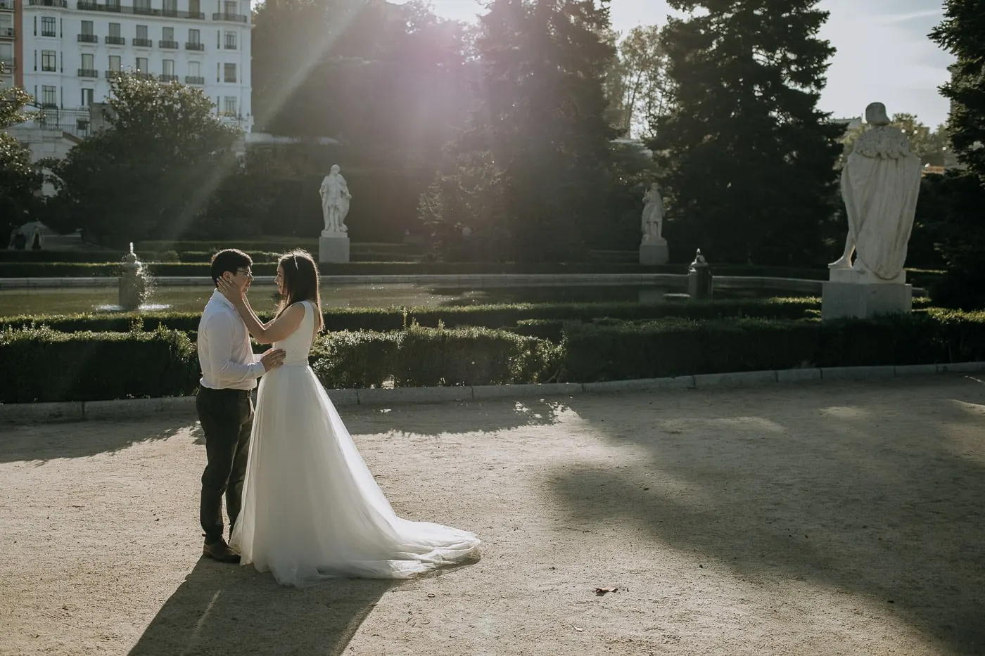 Los novios abrazados en un rayo de sol entre estatuas y parterres, Madrid