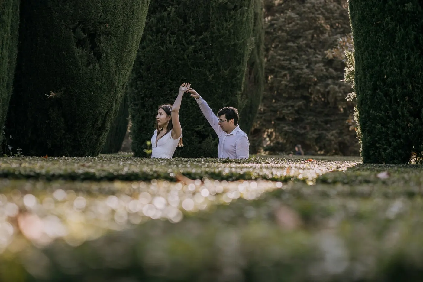 El novio hace girar a la novia entre altos setos de ciprés recortados
