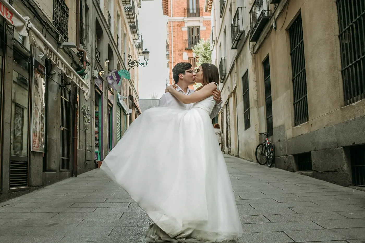 El novio levanta a la novia para besarla en una calle antigua y estrecha