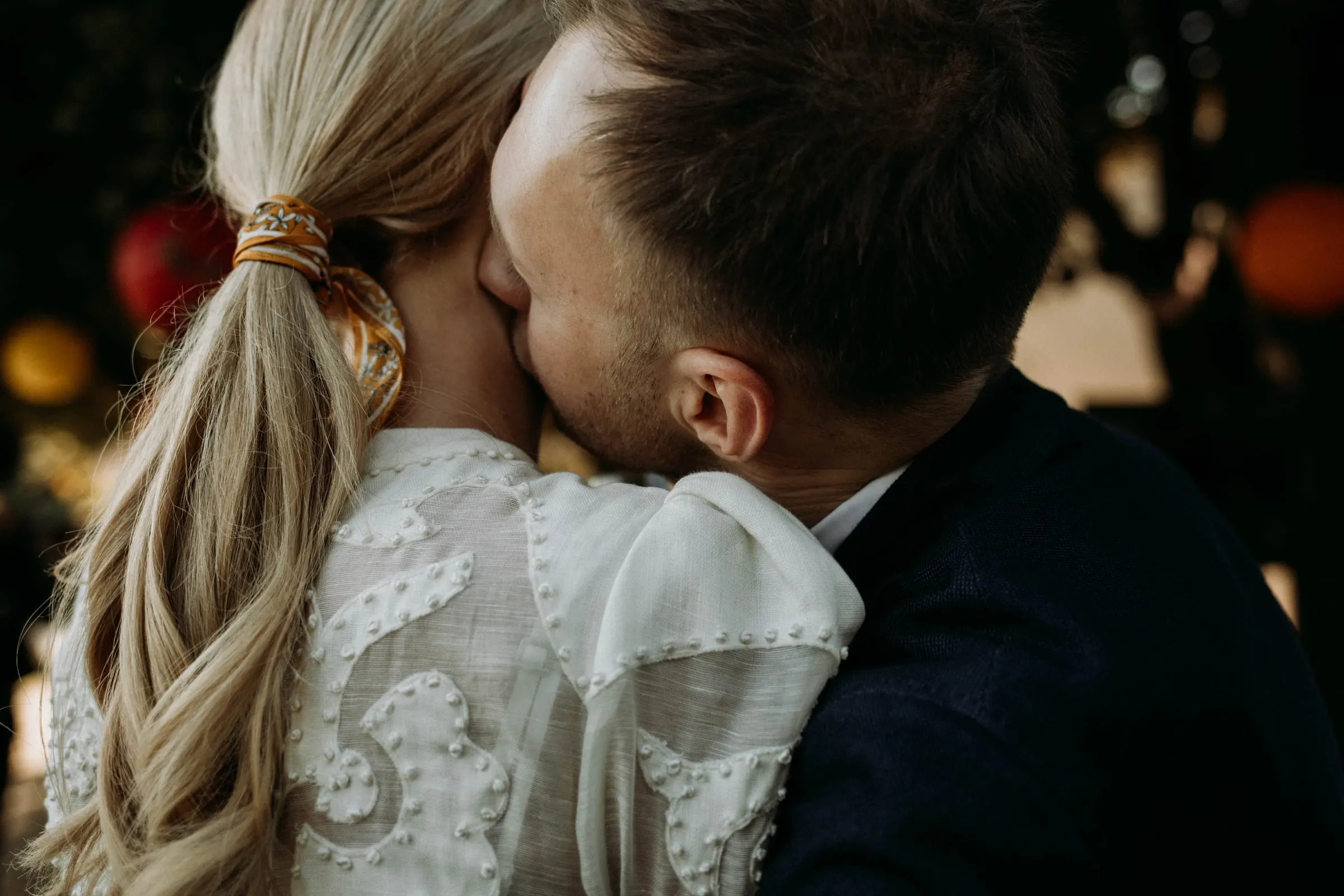El novio besa la mejilla de la novia, con la coleta recogida con un aro dorado, en una masía de Girona