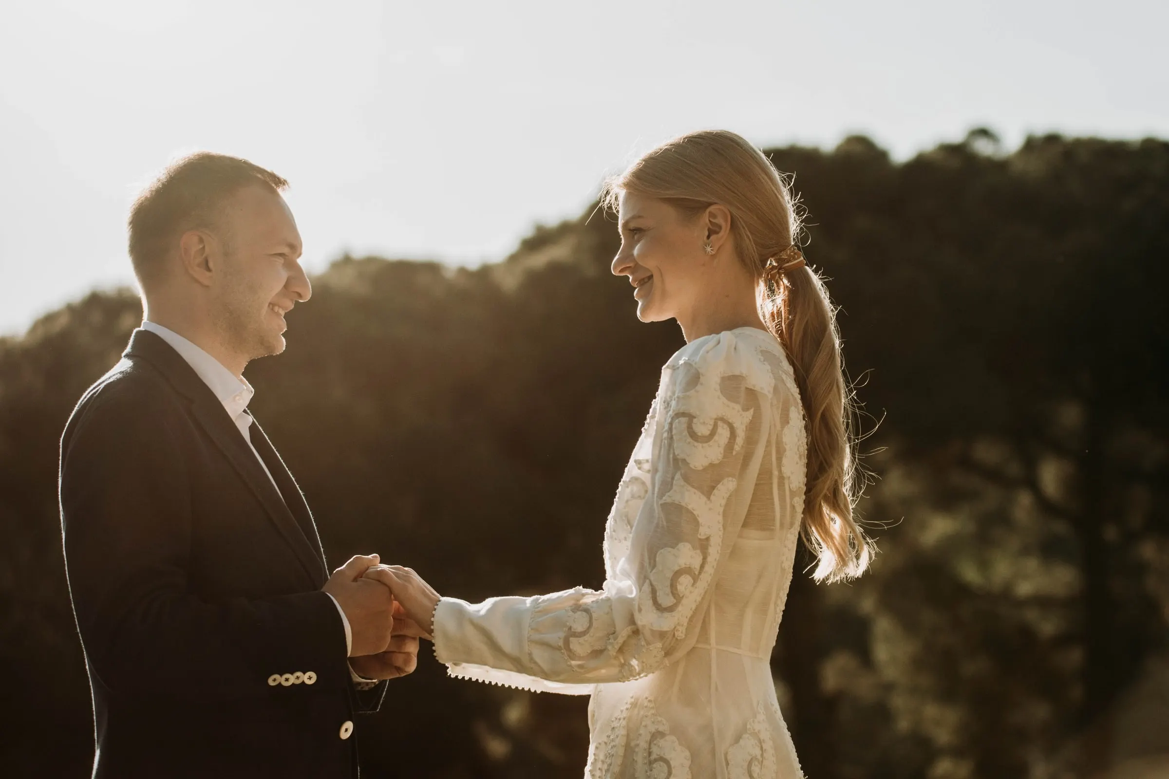 Los novios se cogen de las manos y se sonríen a contraluz en la terraza de una masía de Girona