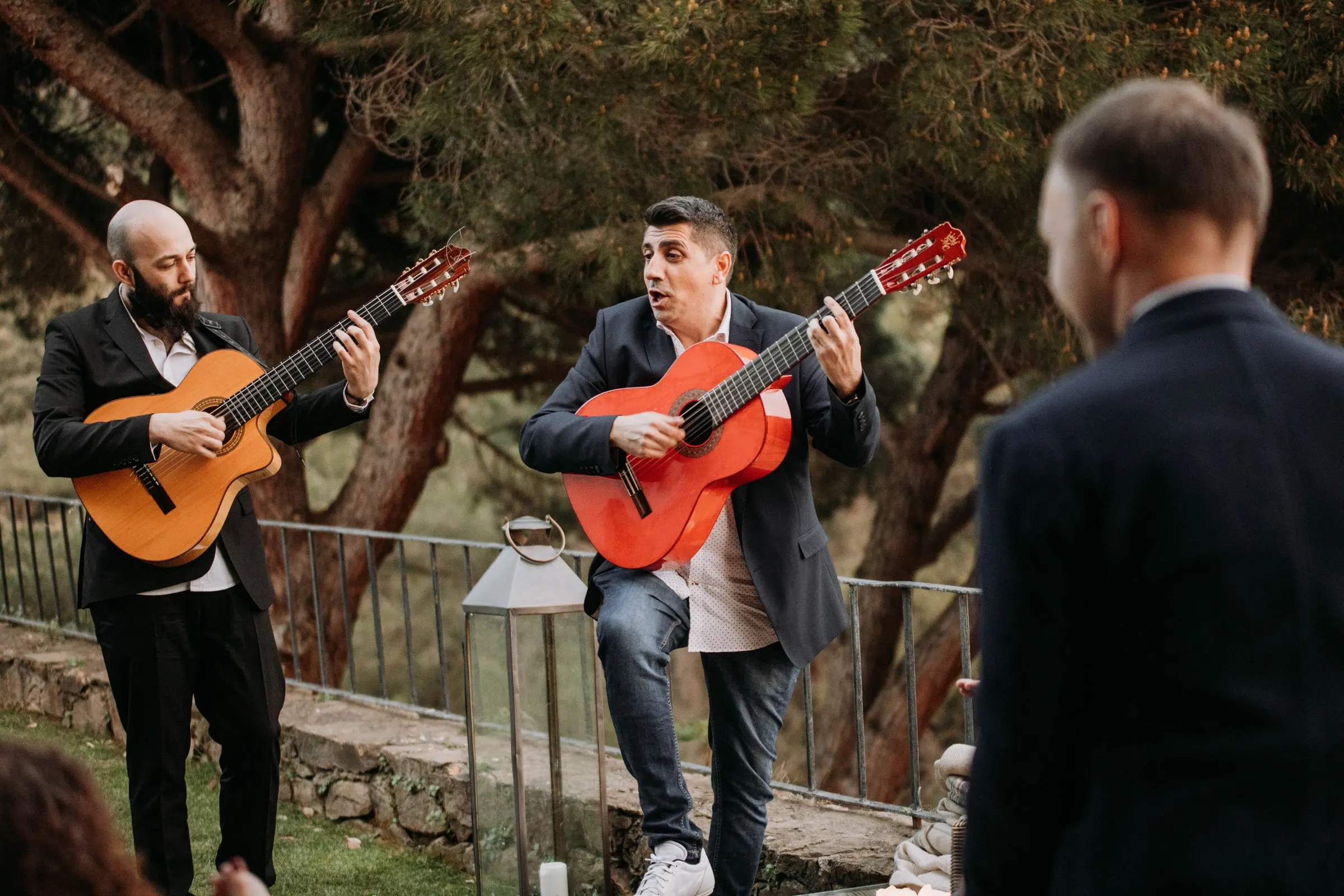 Dos guitarristas tocan en el jardín mientras el novio los mira de espaldas, en una masía de Girona