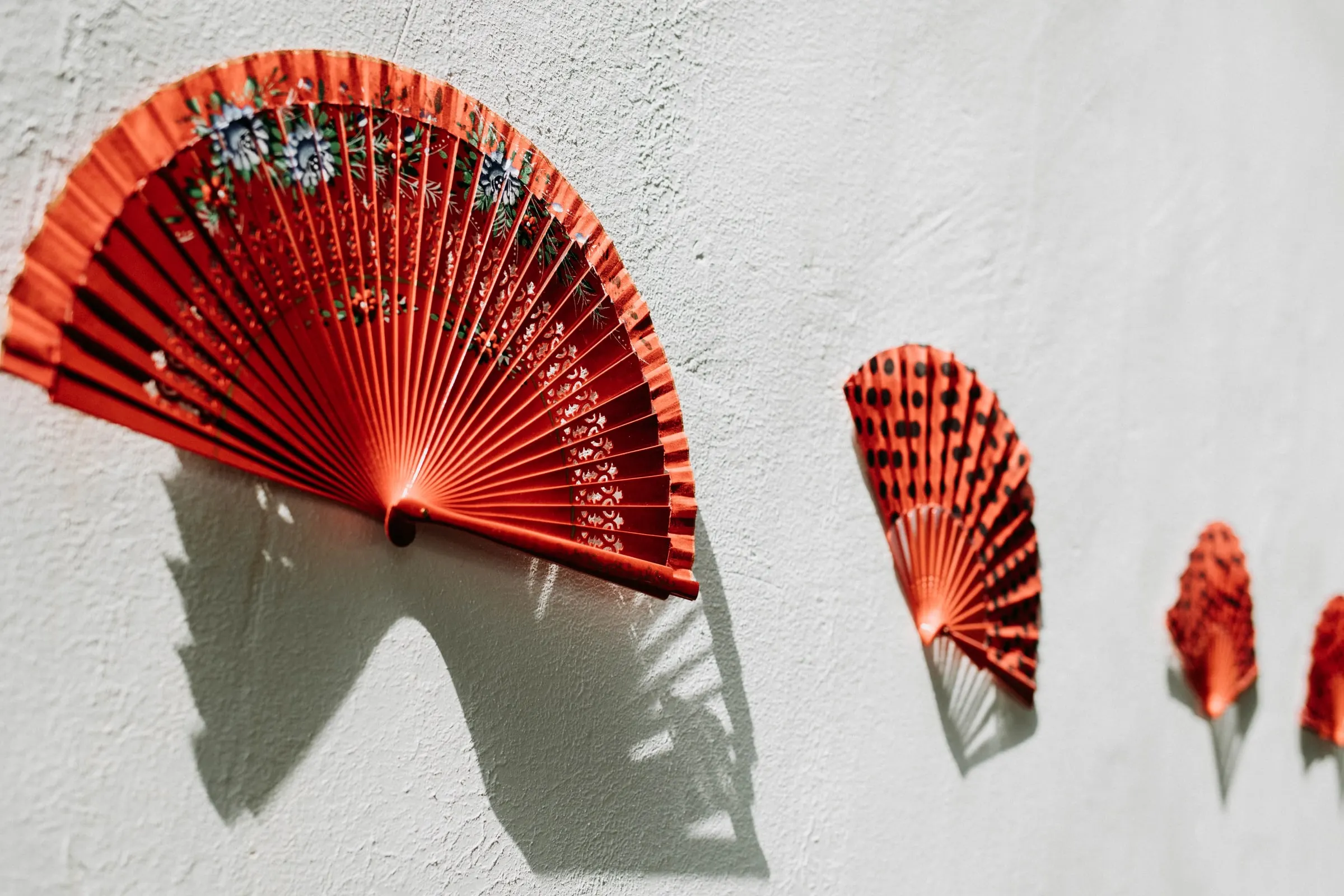 Abanicos rojos colgados en una pared encalada, con sombras nítidas al sol, en una masía de Girona