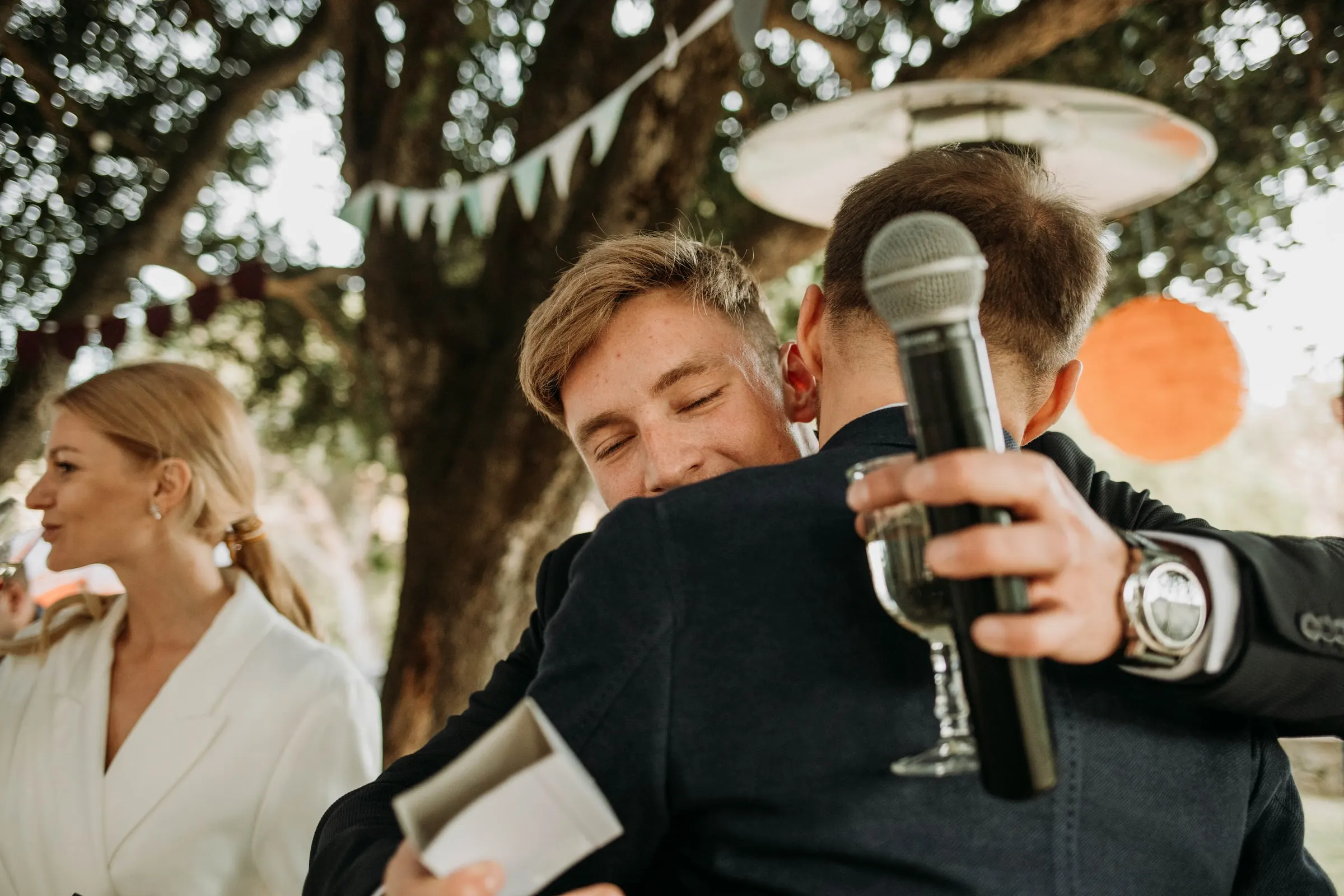 El novio abraza a un invitado con micrófono y copa durante los discursos, en una masía de Girona
