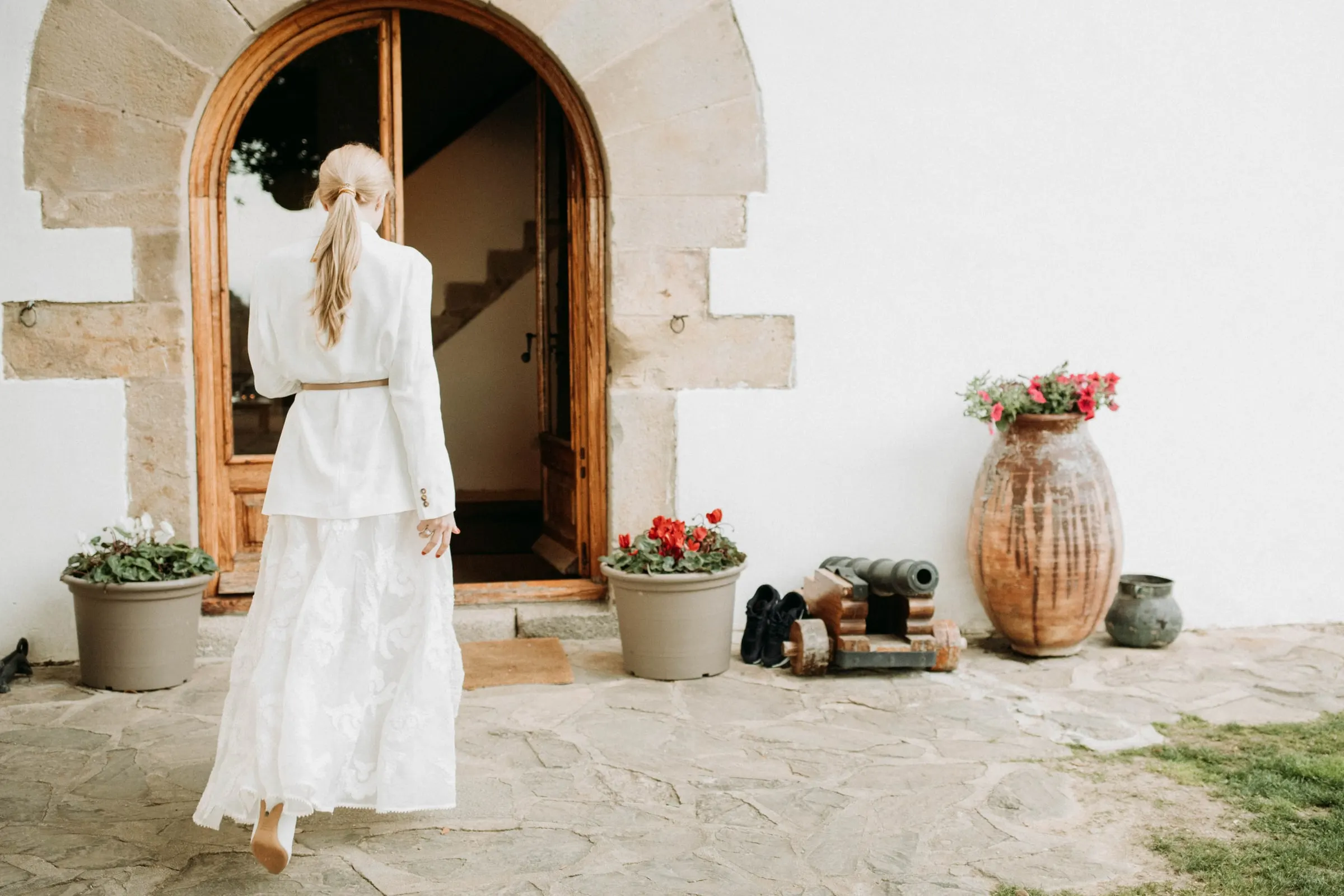La novia, de espaldas, camina hacia la puerta de piedra en arco de una masía de Girona