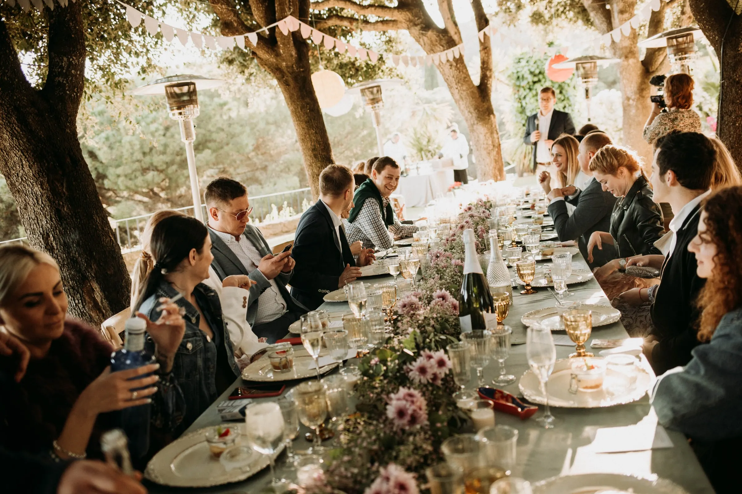 Los invitados charlan a lo largo de la mesa bajo los árboles durante la comida en una masía de Girona