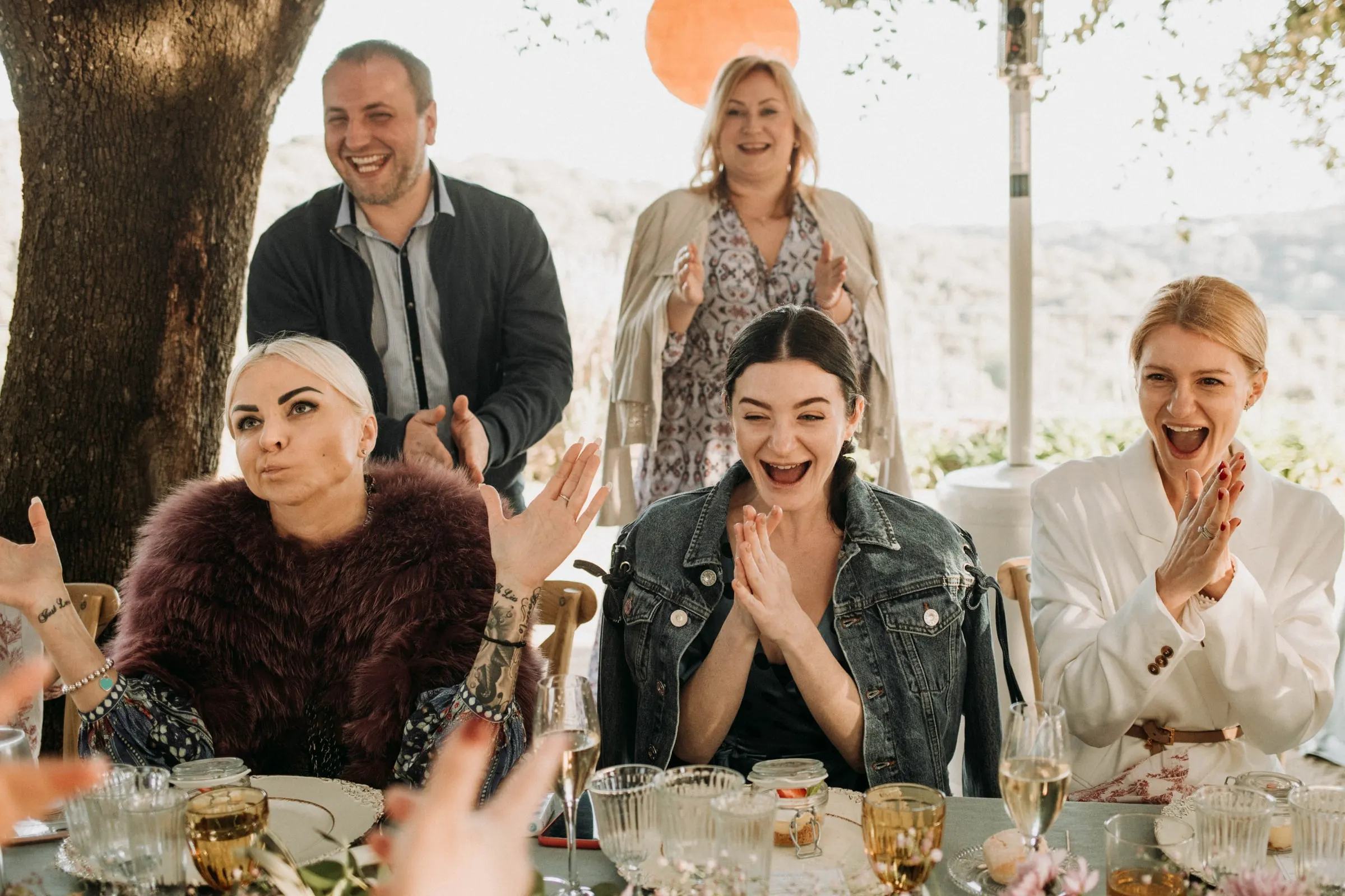 Los invitados aplauden y celebran en la mesa, con la novia sonriendo entre ellos, en una masía de Girona