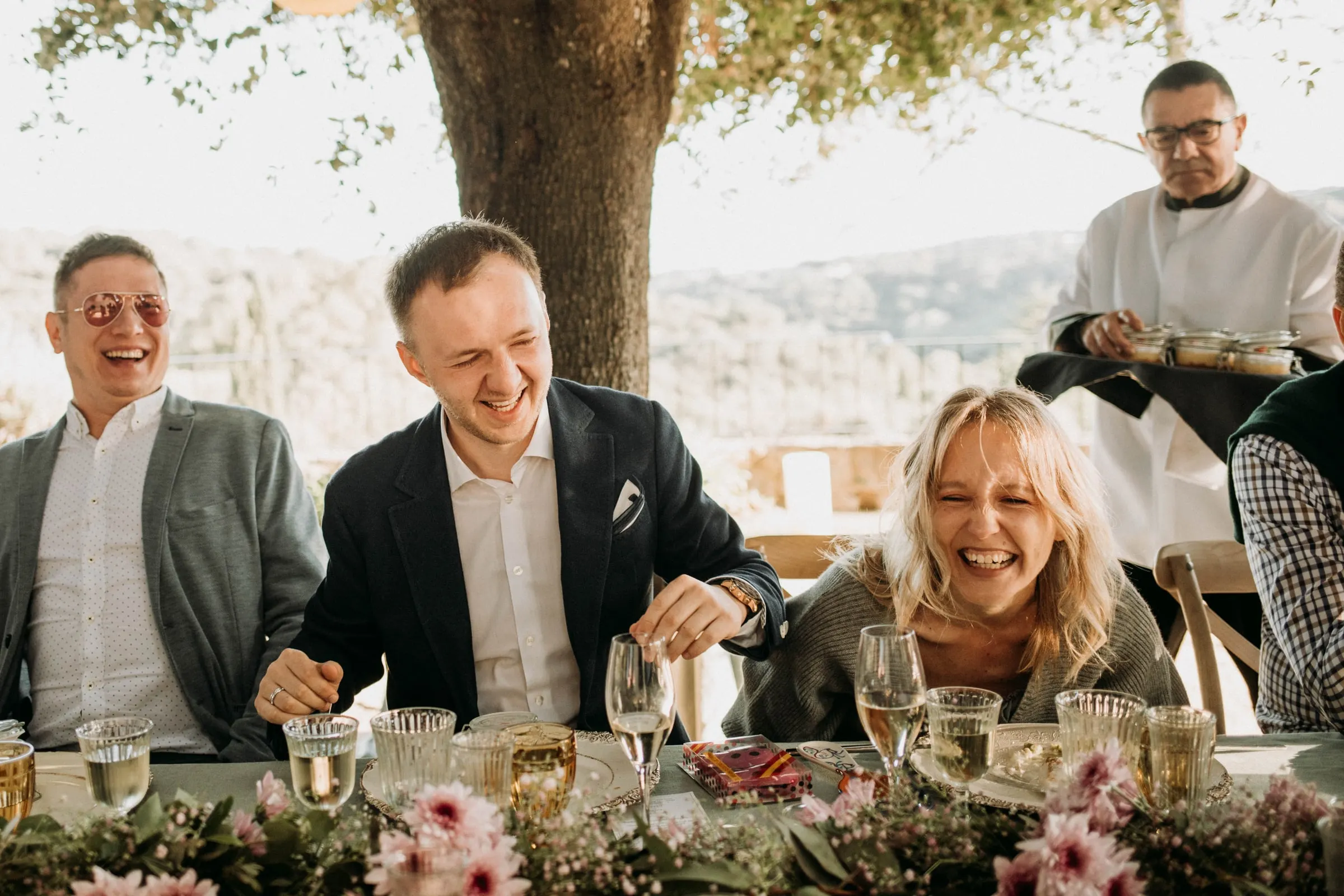 El novio y los invitados se ríen a carcajadas en la mesa de la comida, en una masía de Girona