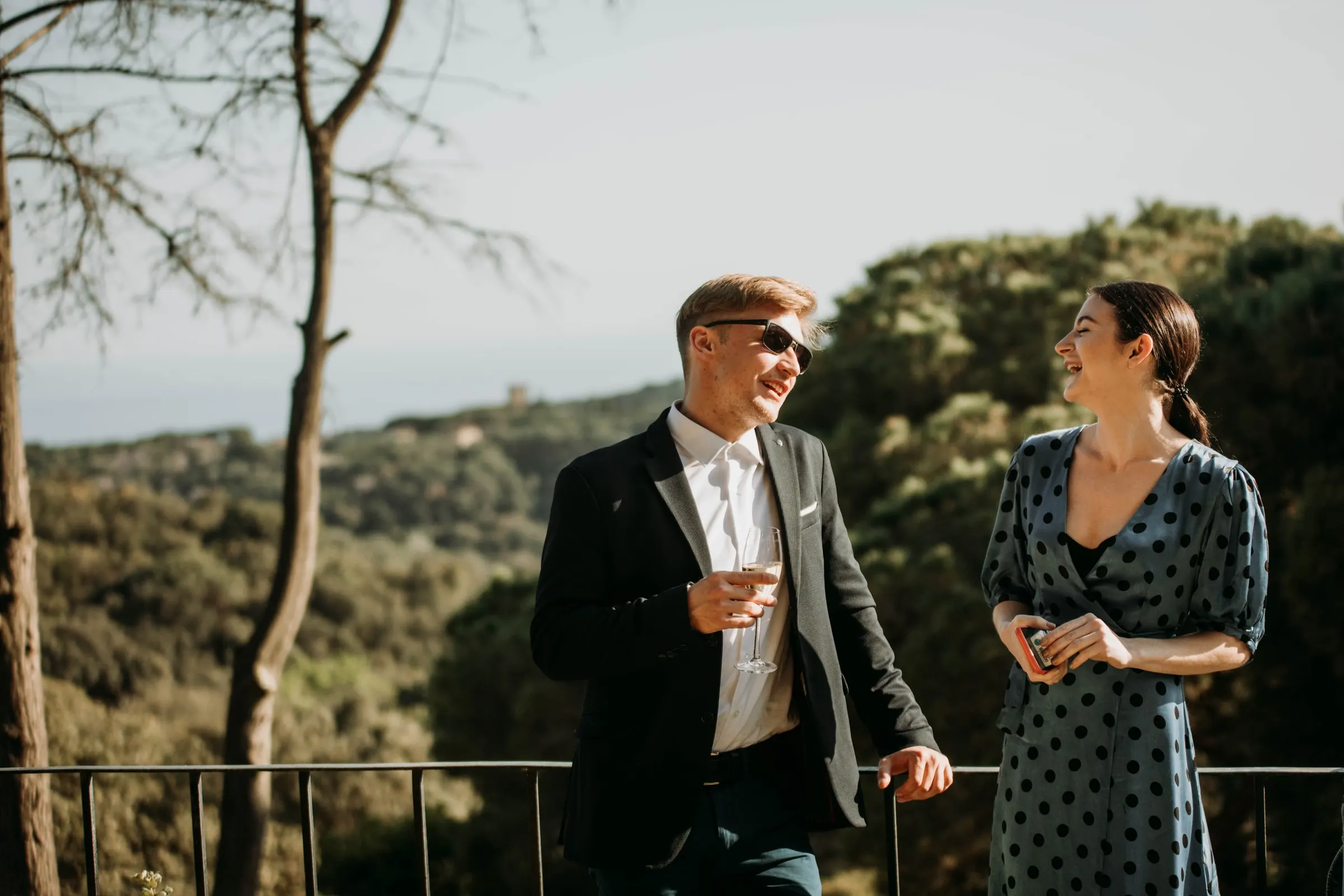 Dos invitados charlan junto a la barandilla con vistas a las colinas boscosas de una masía de Girona