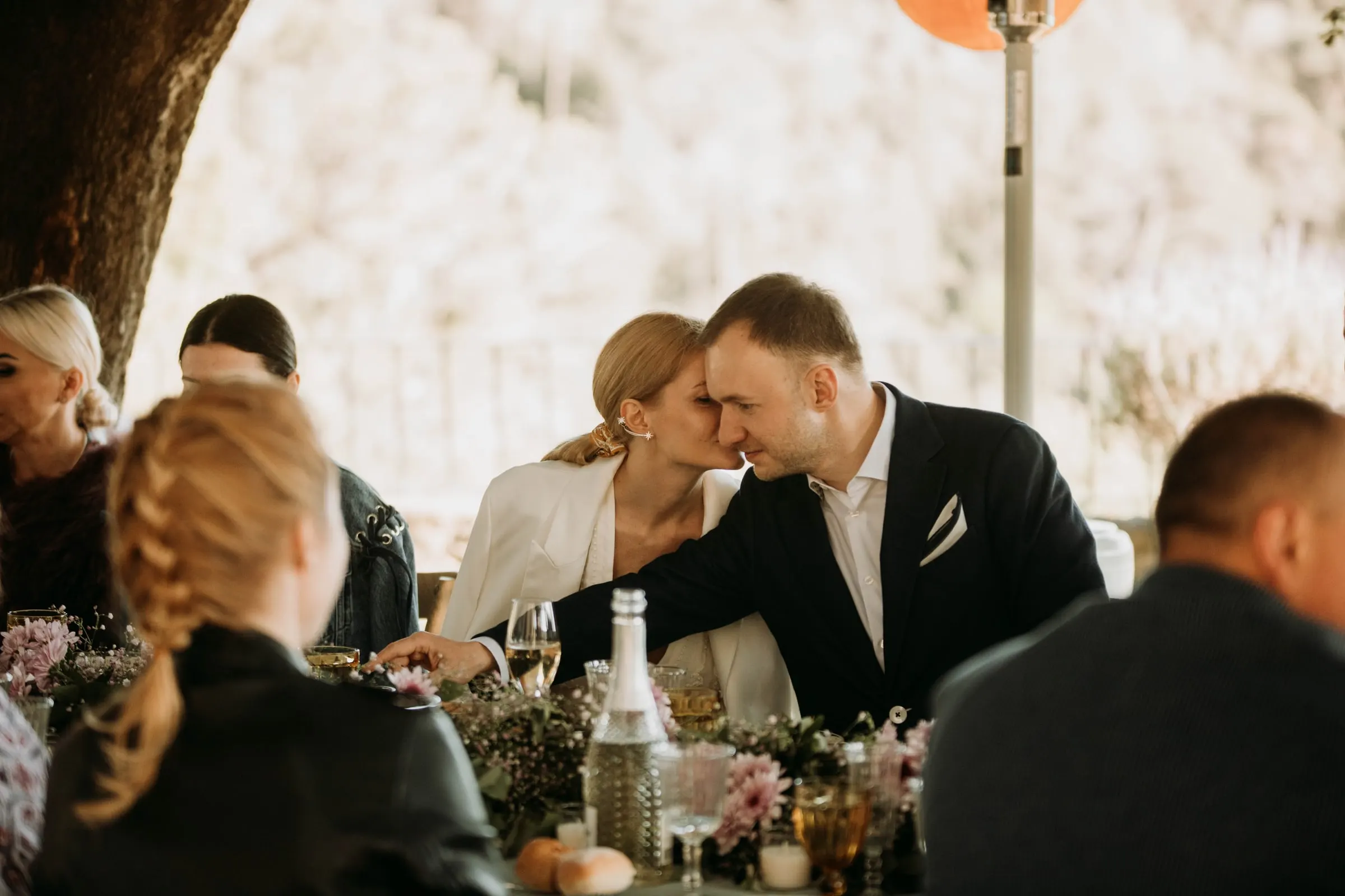 El novio se inclina para besar a la novia en la mesa, entre los invitados, en una masía de Girona