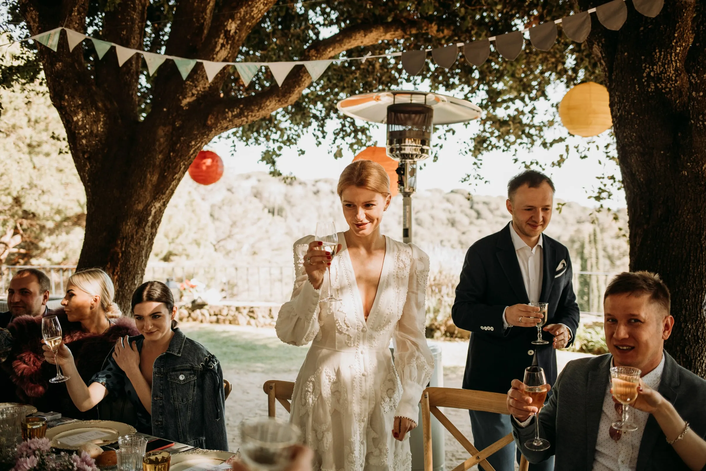 La novia, de pie, propone un brindis mientras los invitados celebran bajo farolillos, en una masía de Girona