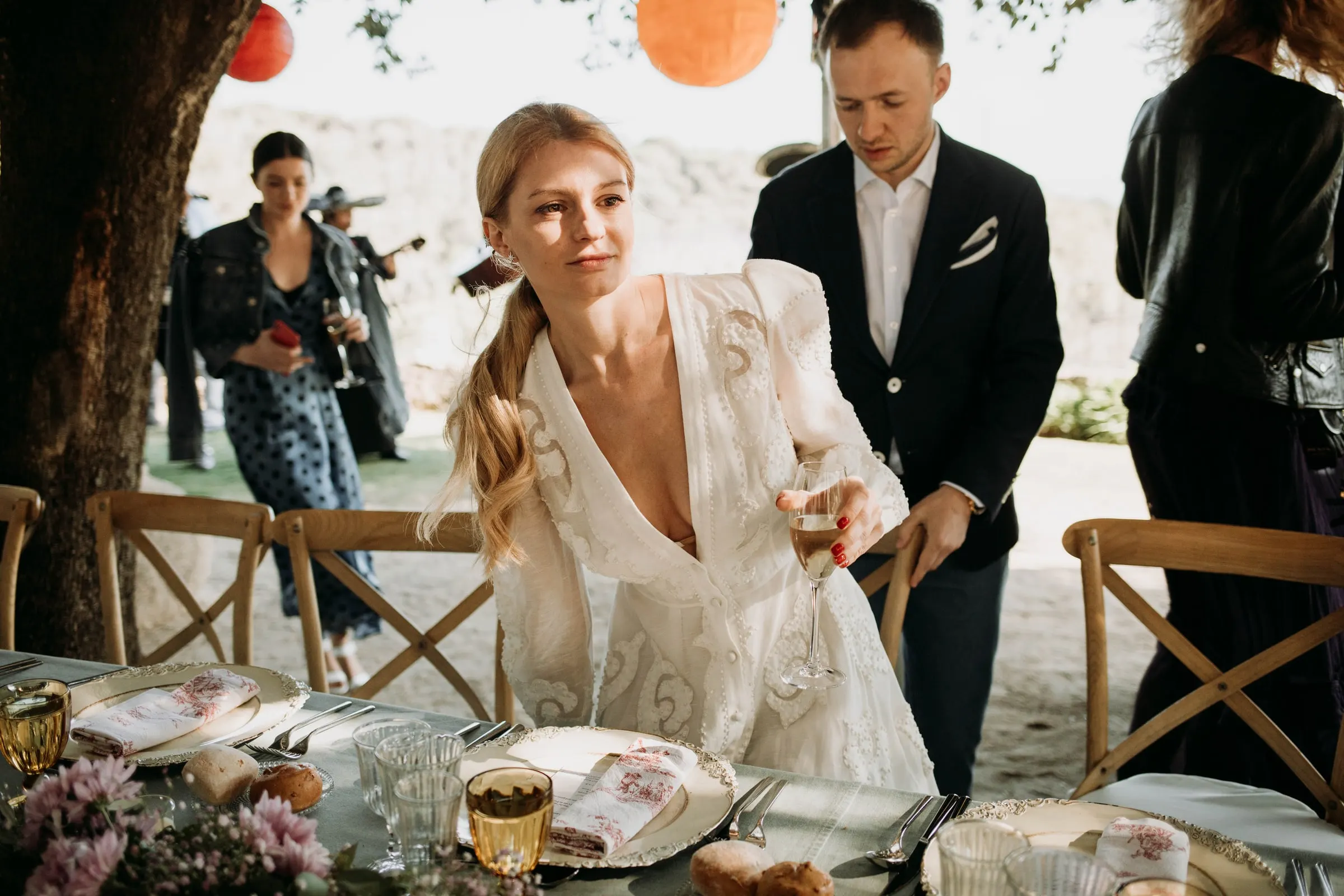 La novia se sienta a la mesa del banquete mientras el novio aparta su silla, en una masía de Girona