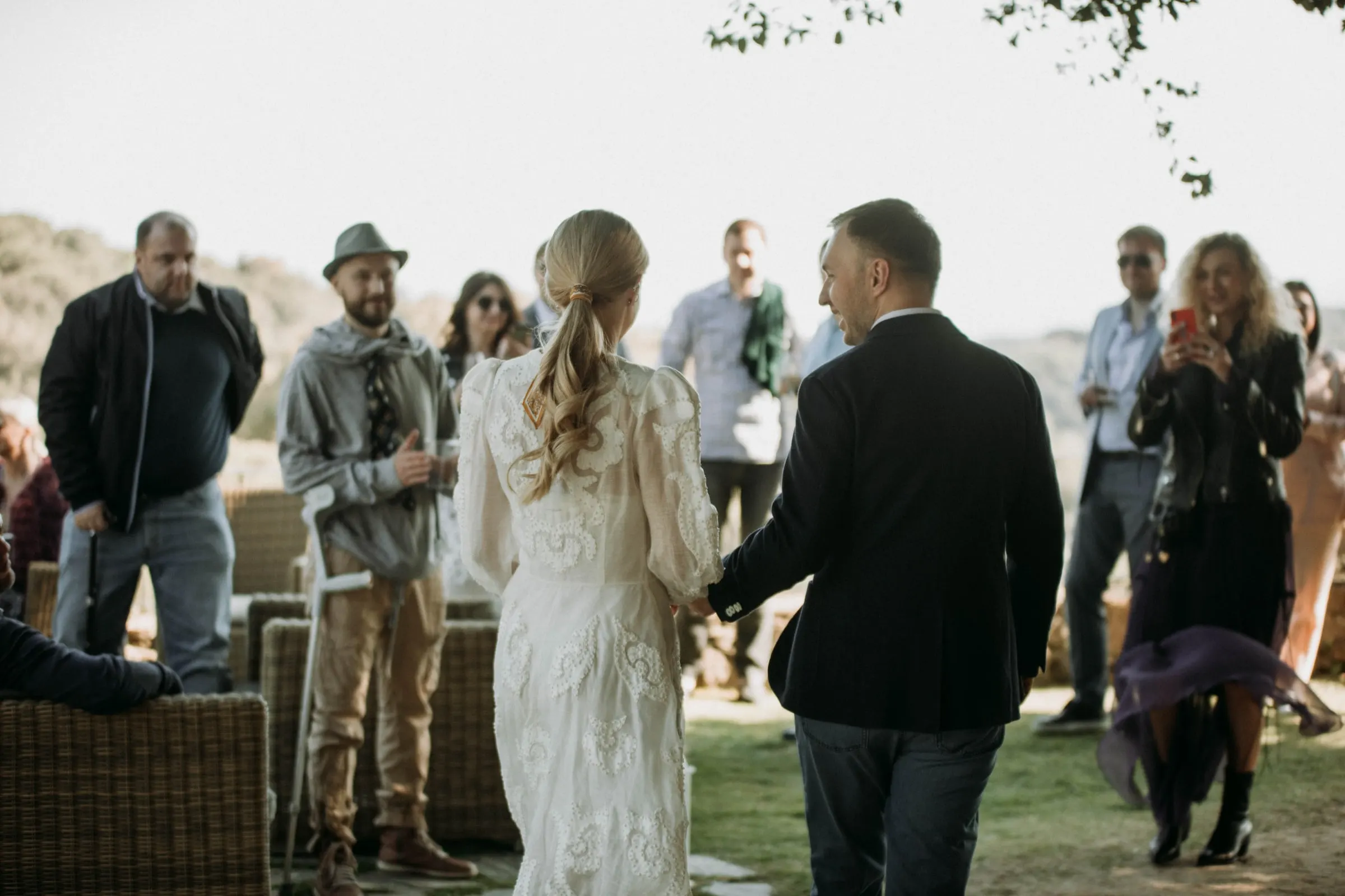 Los novios, de espaldas, avanzan de la mano entre sus invitados en una masía de Girona