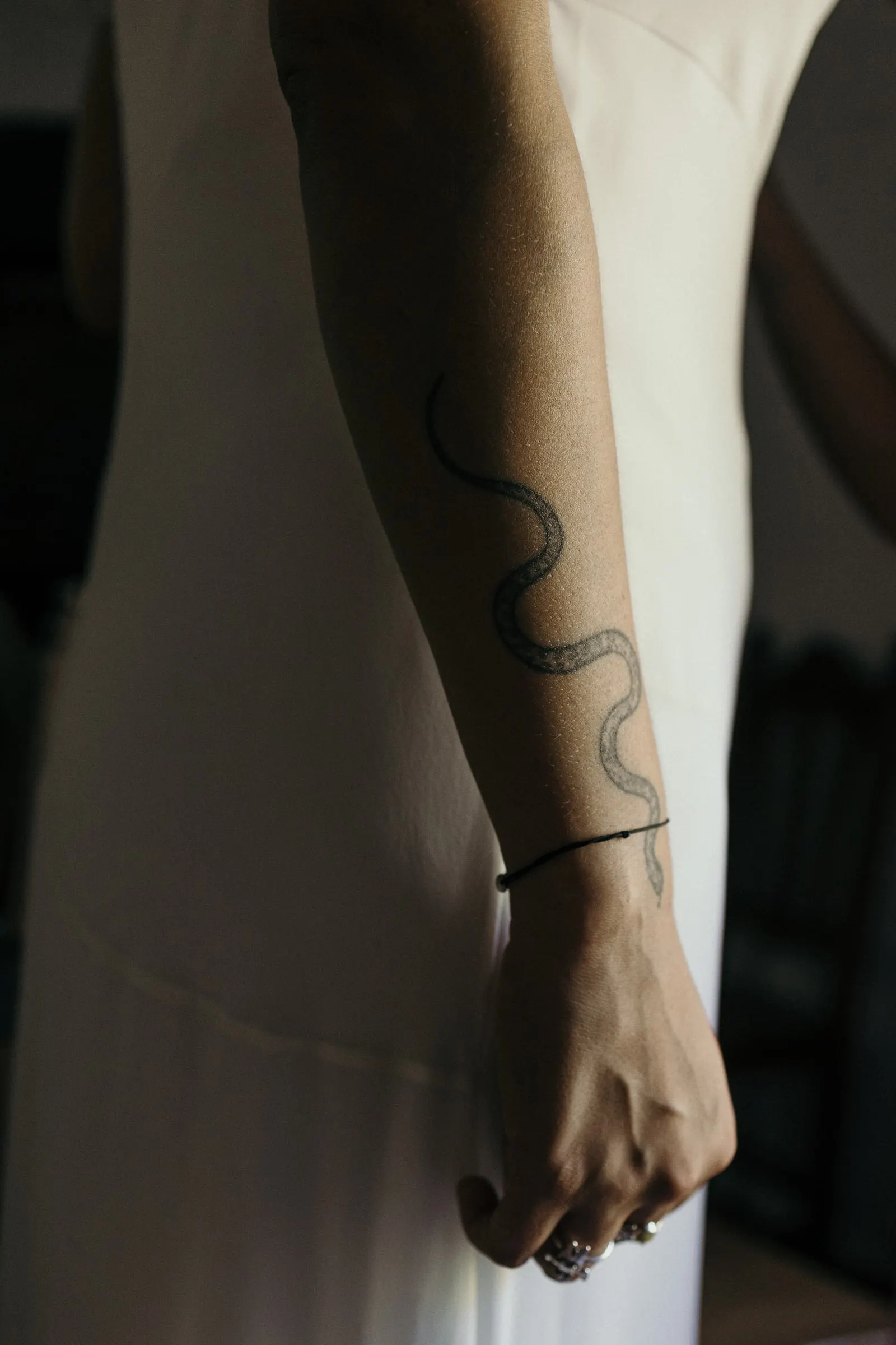 Tatuaje de serpiente en el brazo de la novia sobre su vestido blanco de seda