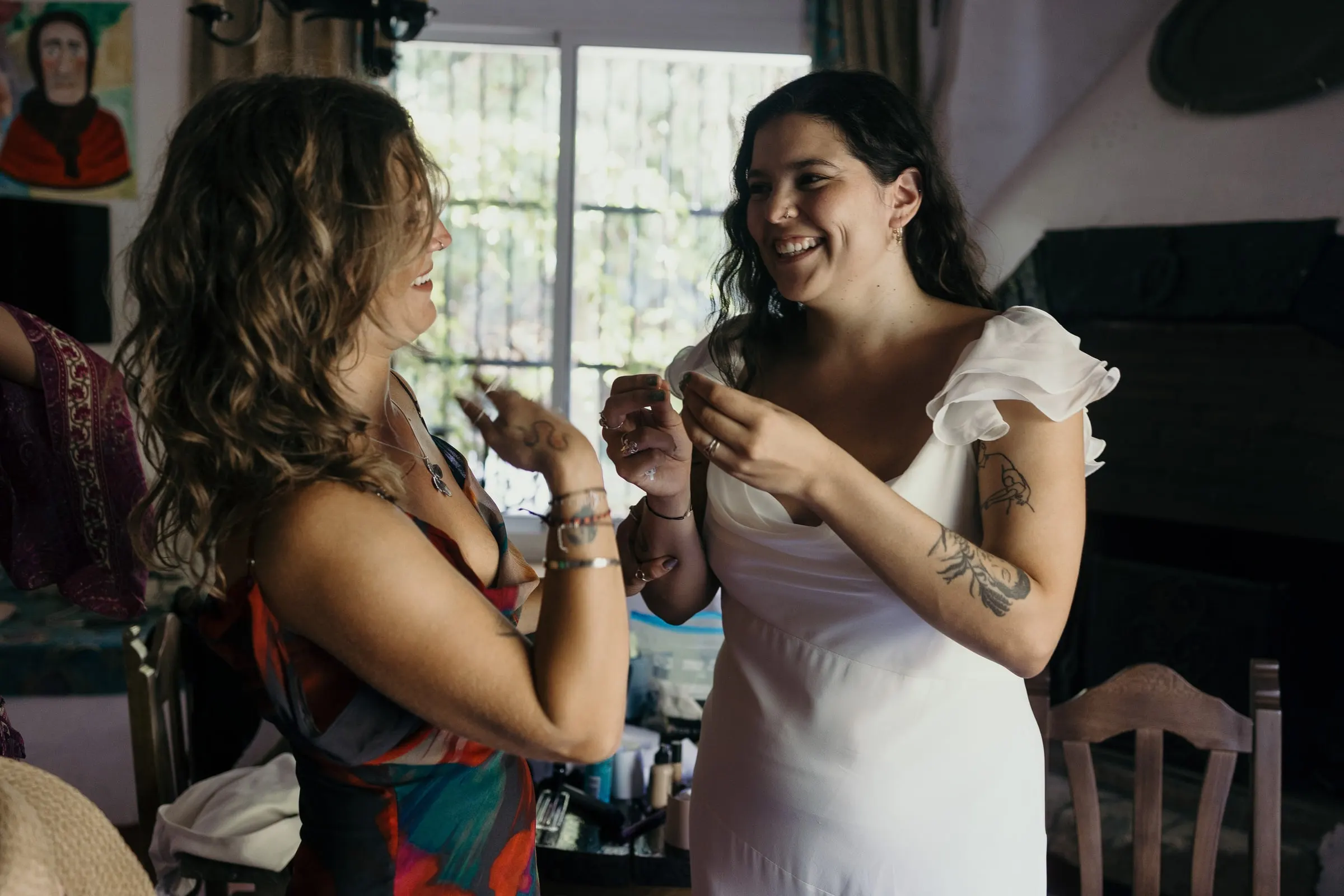 La novia se ríe con una amiga de vestido estampado mientras se prepara