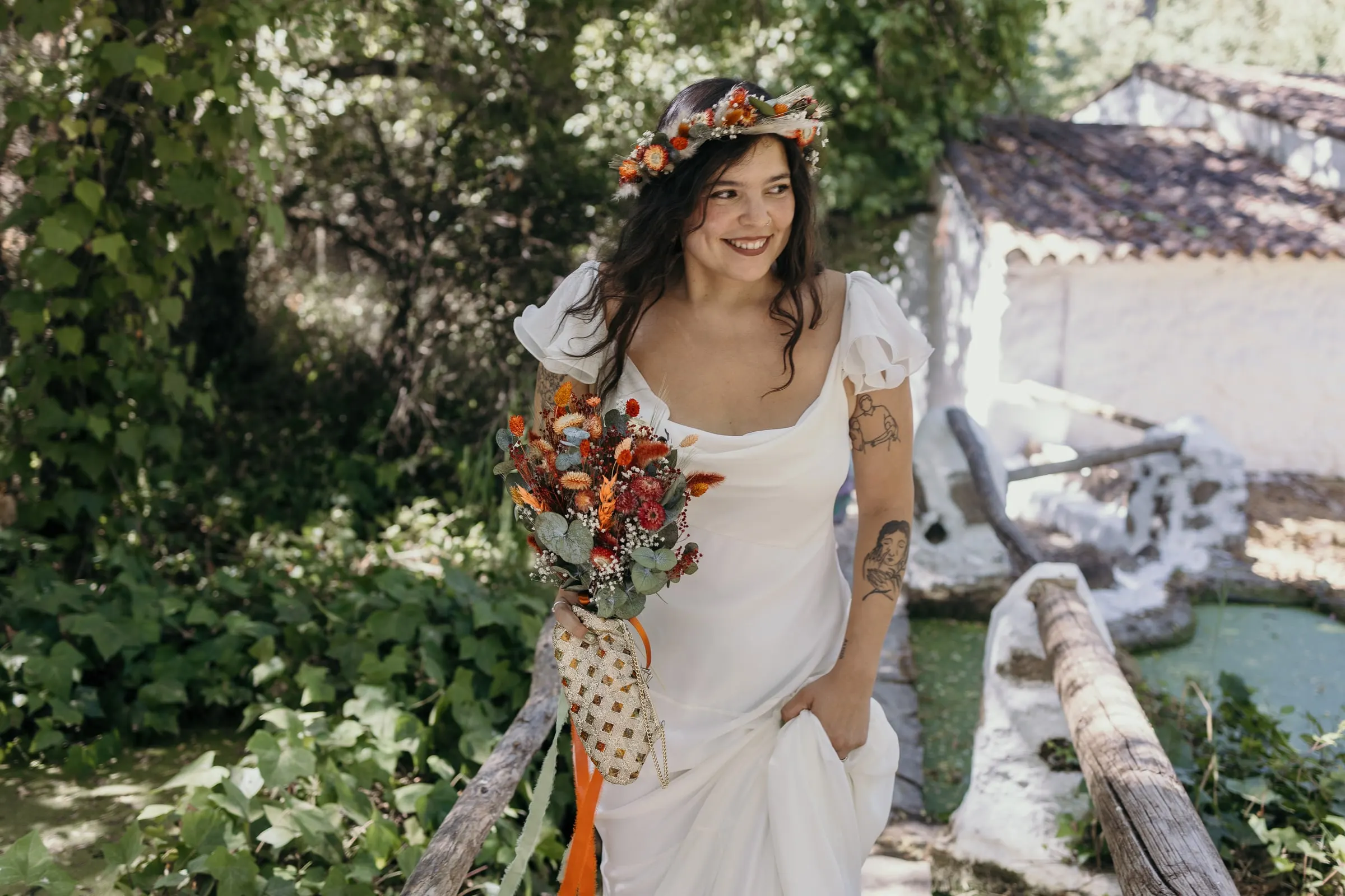 La novia se ríe junto a la baranda de madera del canal del molino, con una casa encalada detrás, en Molino La Flor