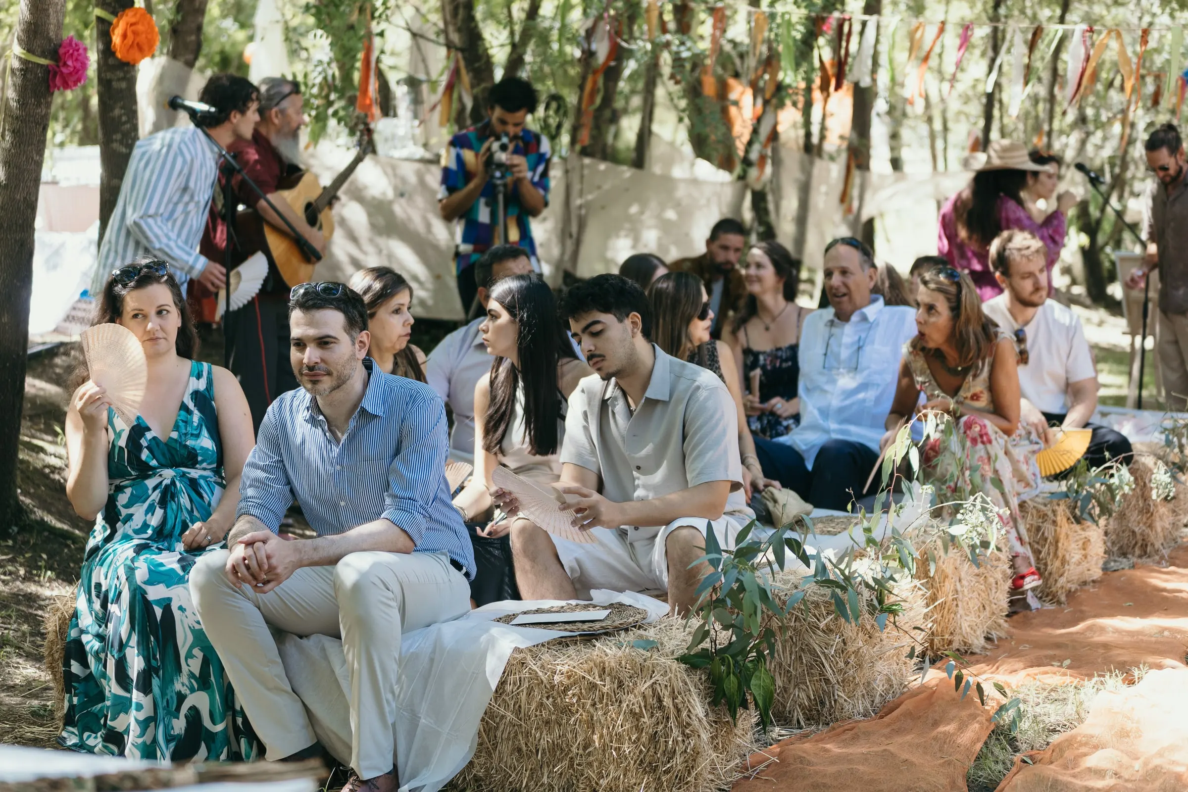 Guests seated on hay bales under ribbon garlands in the woods at Molino La Flor