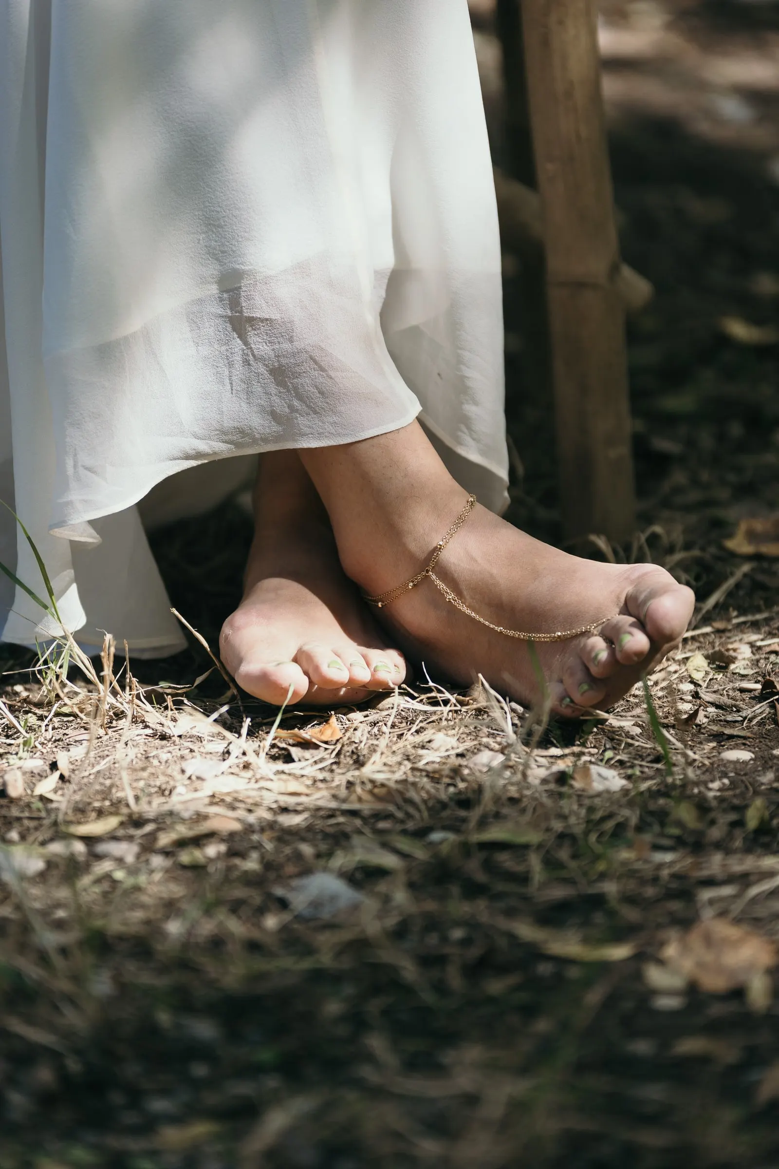 Los pies descalzos de la novia con una tobillera sobre la hierba seca
