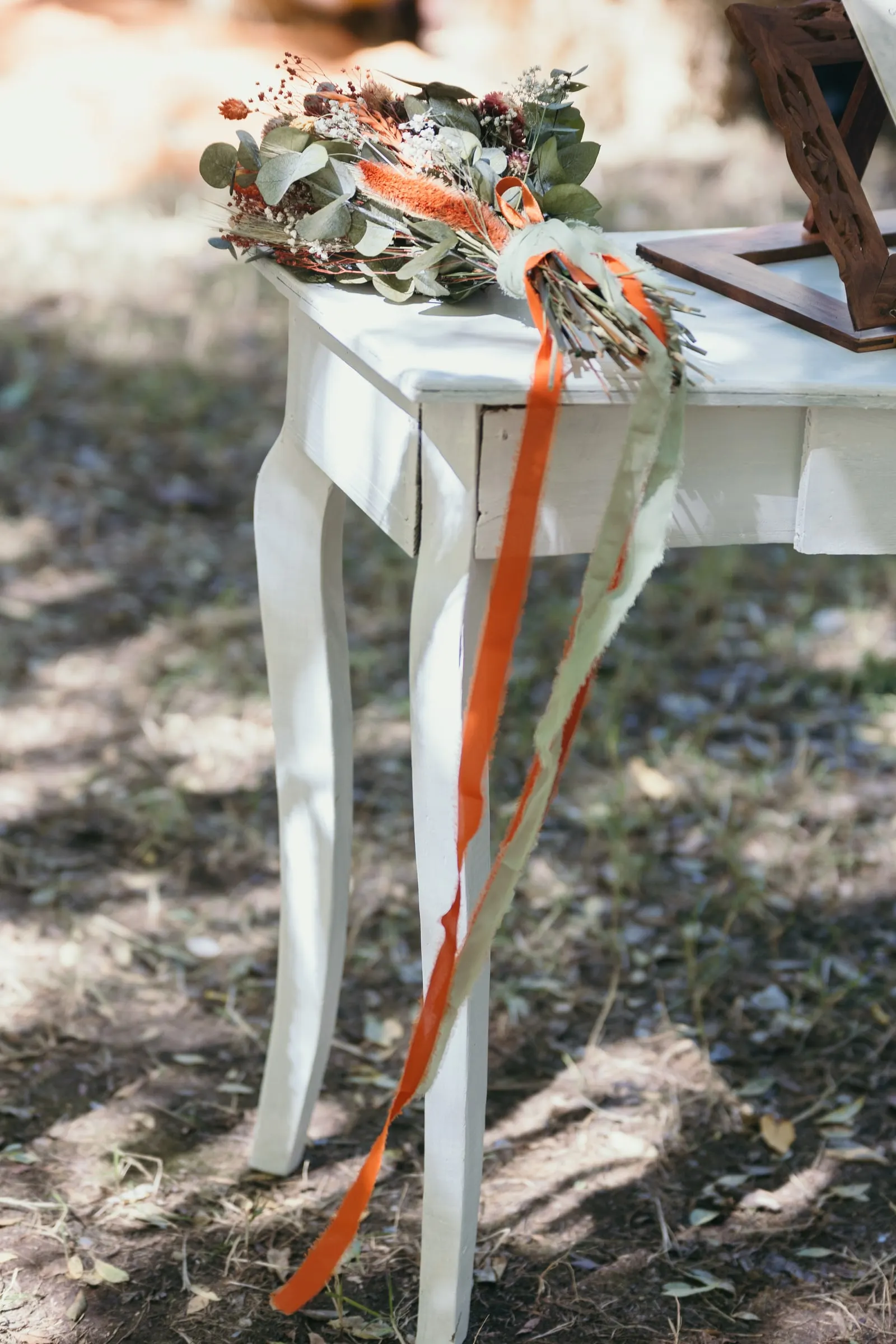 Ramo de flores secas con cintas naranjas sobre una mesa blanca de ceremonia