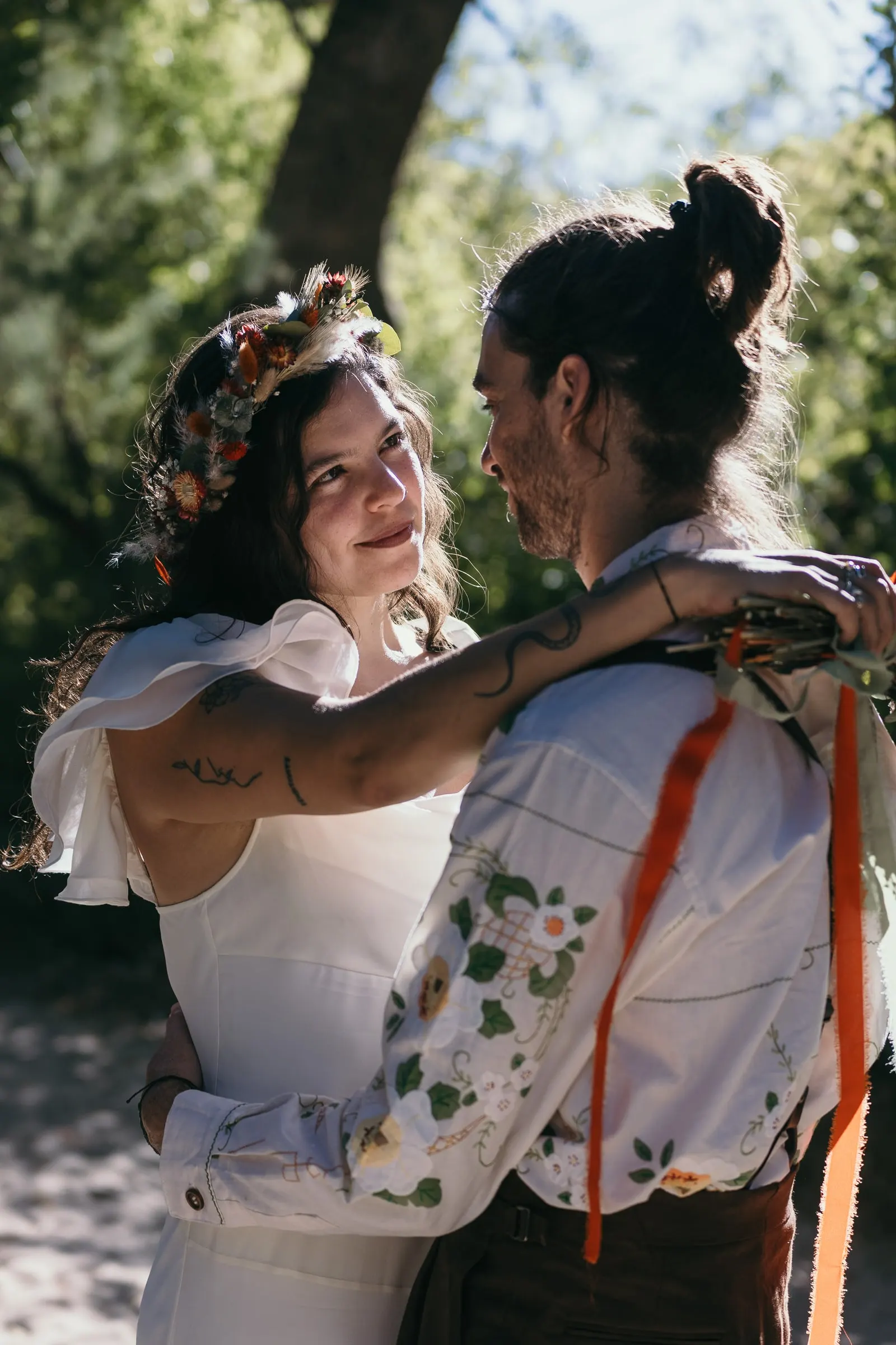 La novia rodea con el brazo el cuello del novio a la sombra de los árboles