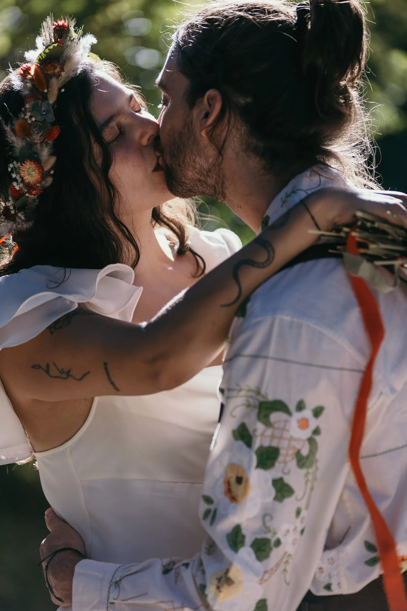 Beso en primer plano, con su corona de flores y la camisa bordada de él a la luz