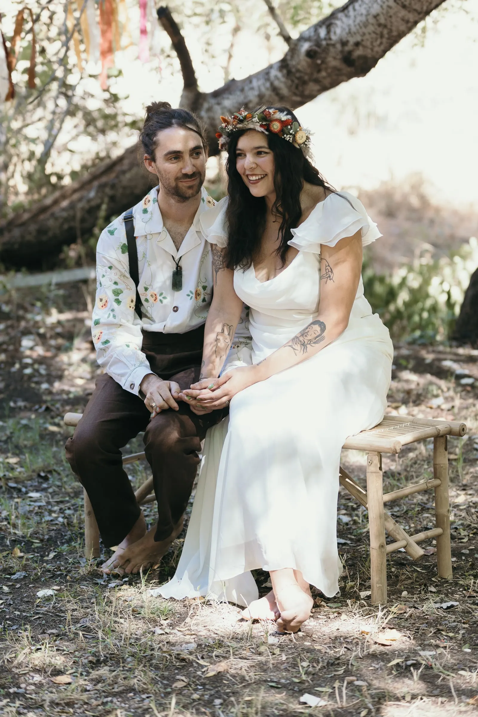 Los novios sentados juntos en un banco de madera, sonrientes durante la ceremonia en el bosque de Molino La Flor