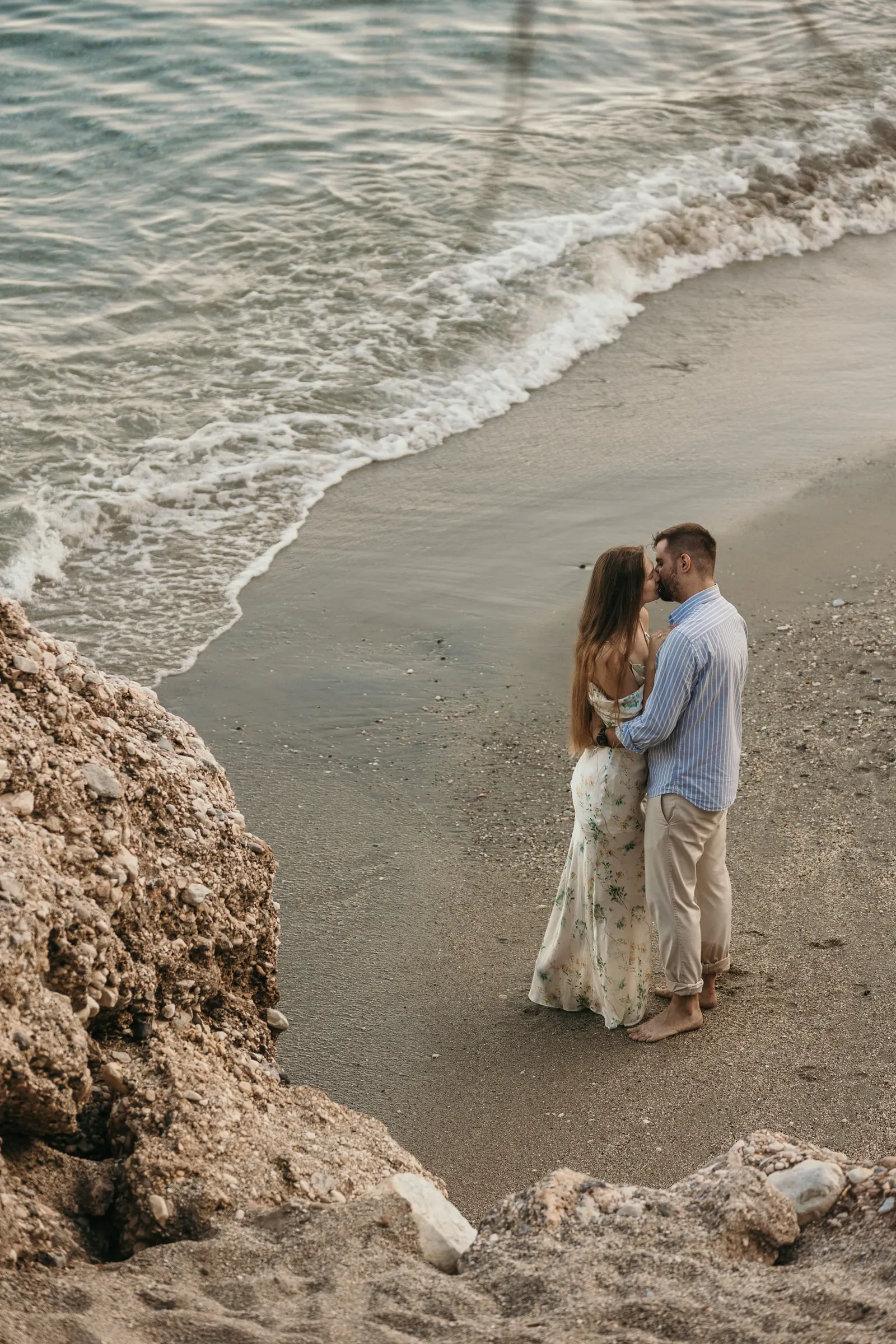 La pareja abrazada en la orilla junto a las rocas, vista desde arriba, en la playa de Nerja