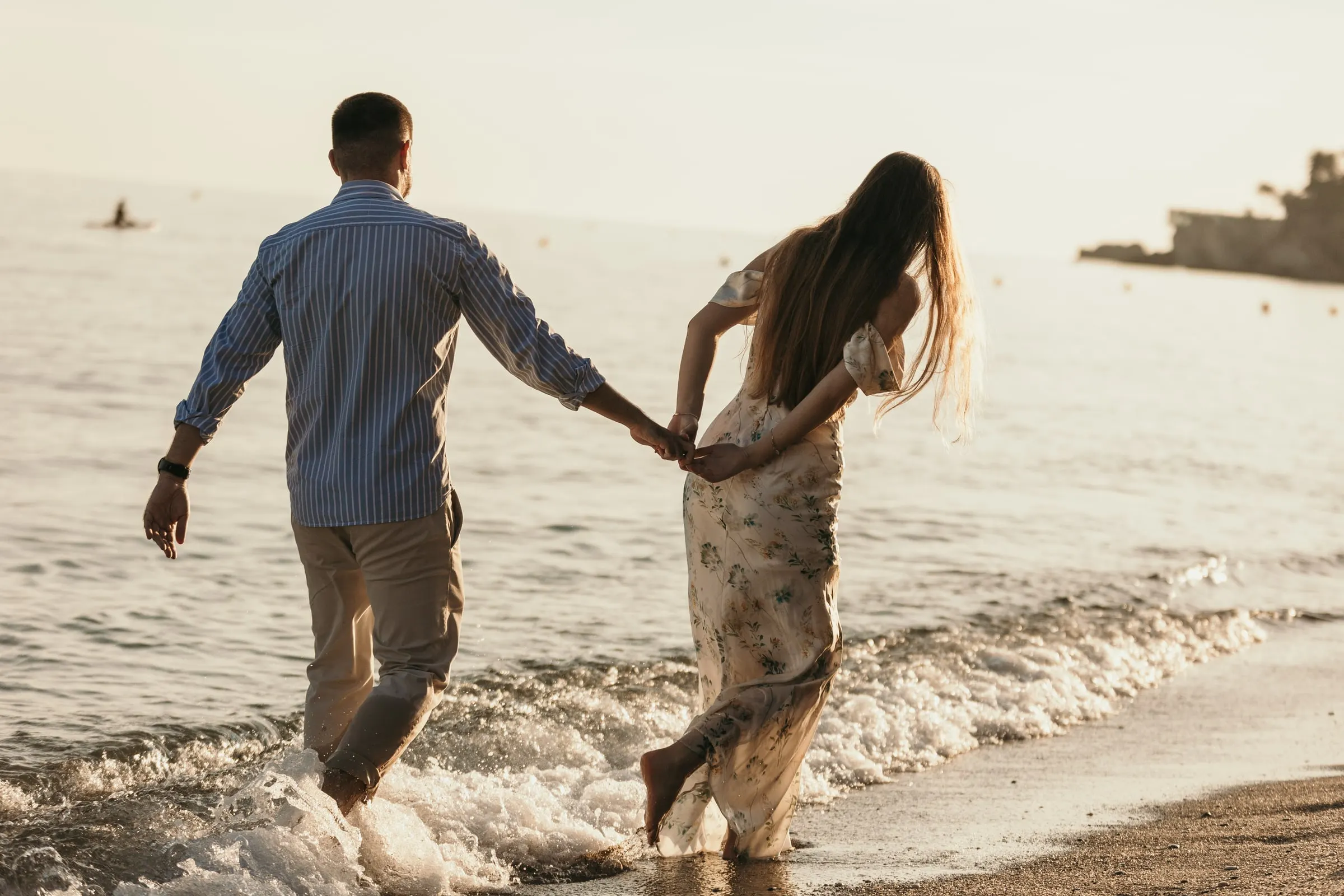 La pareja corre de la mano hacia las olas, vista de espaldas, en la playa de Nerja